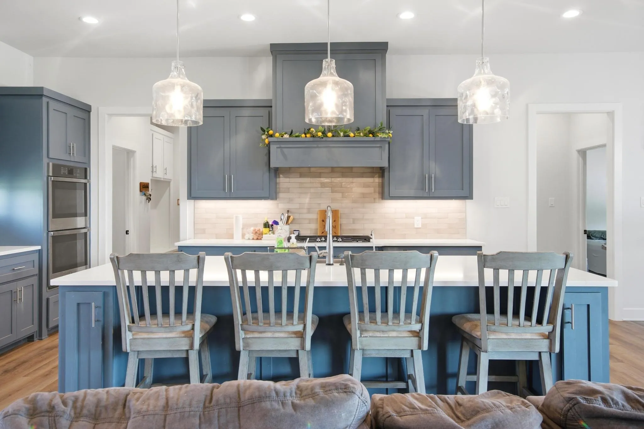 Kitchen featuring an island with seating, a white countertop, blue cabinetry, stainless steel double ovens, and a tile backsplash