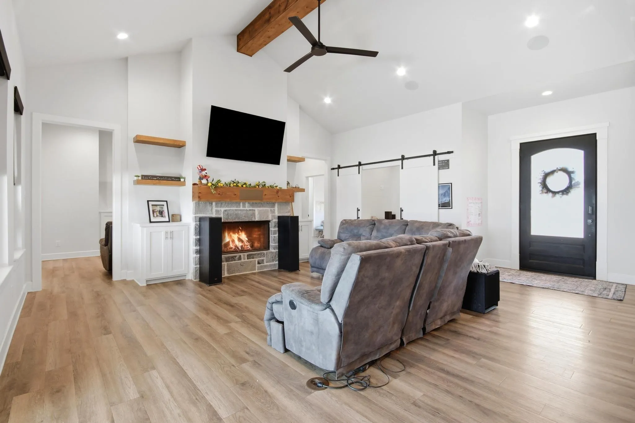 Spacious living area featuring a stone fireplace with a wood mantle, vaulted ceiling with exposed beam, and recessed lighting