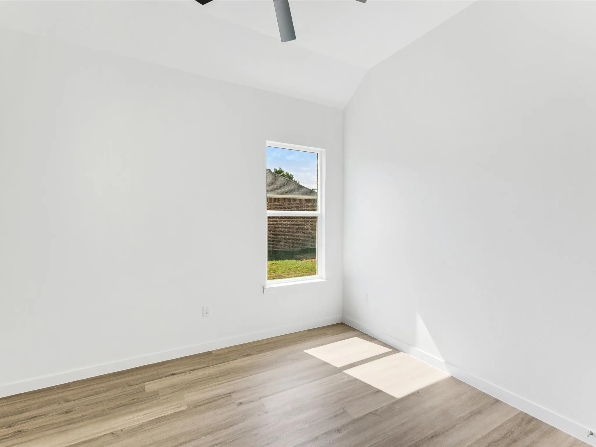 Vaulted ceiling, wood-finish flooring, white walls, and a single window