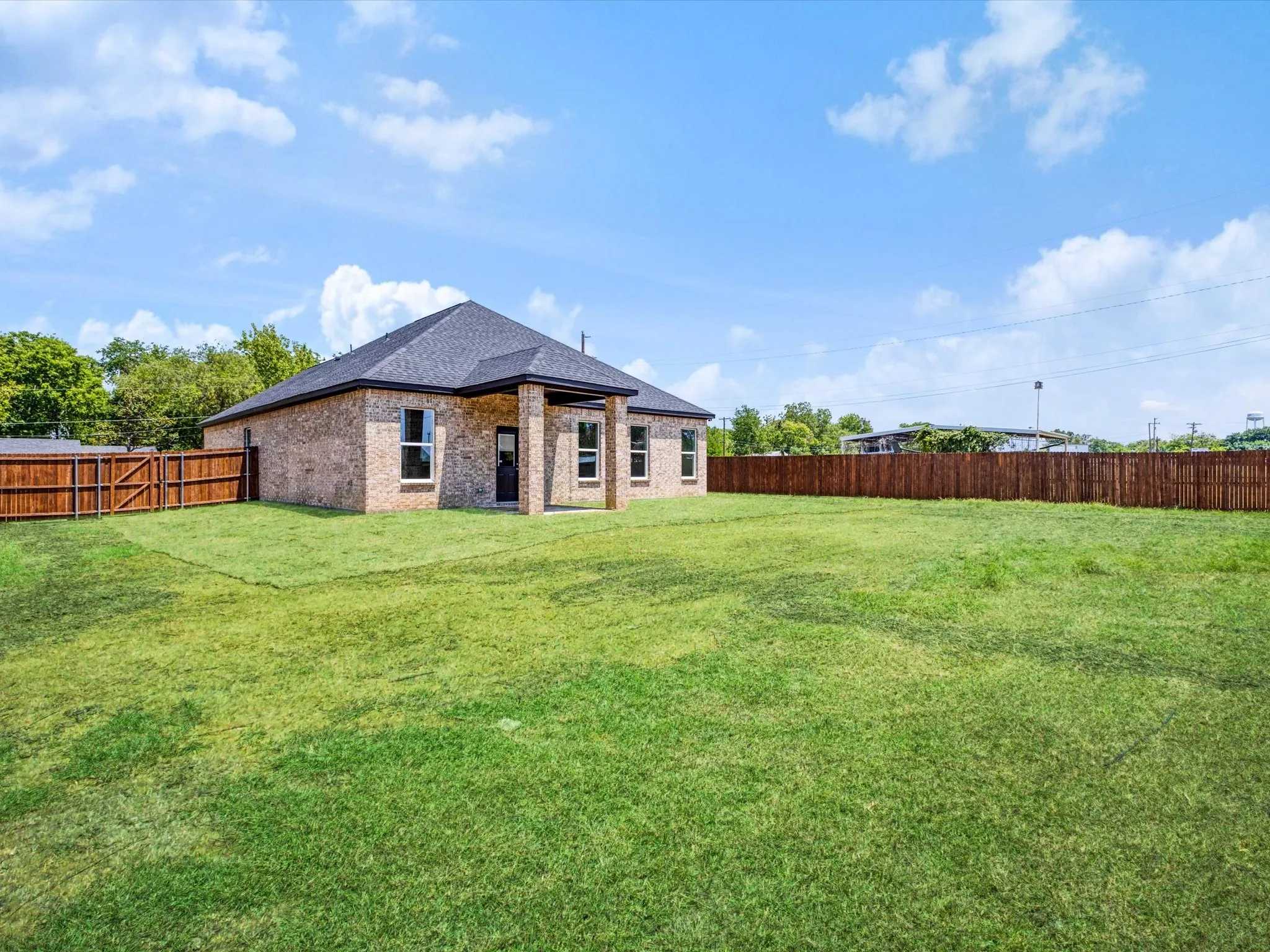 Brick exterior with a dark shingle roof, featuring a covered patio with columns, and a private fenced yard