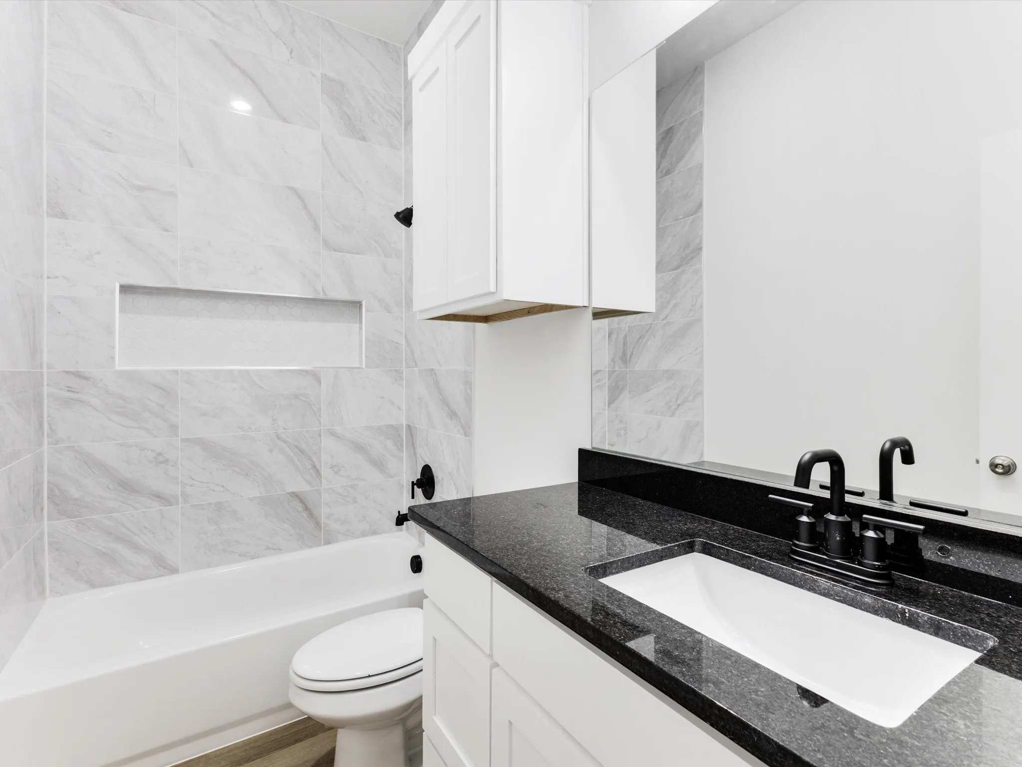 White bathtub with a tiled surround, integrated shower niche, and matte black fixtures