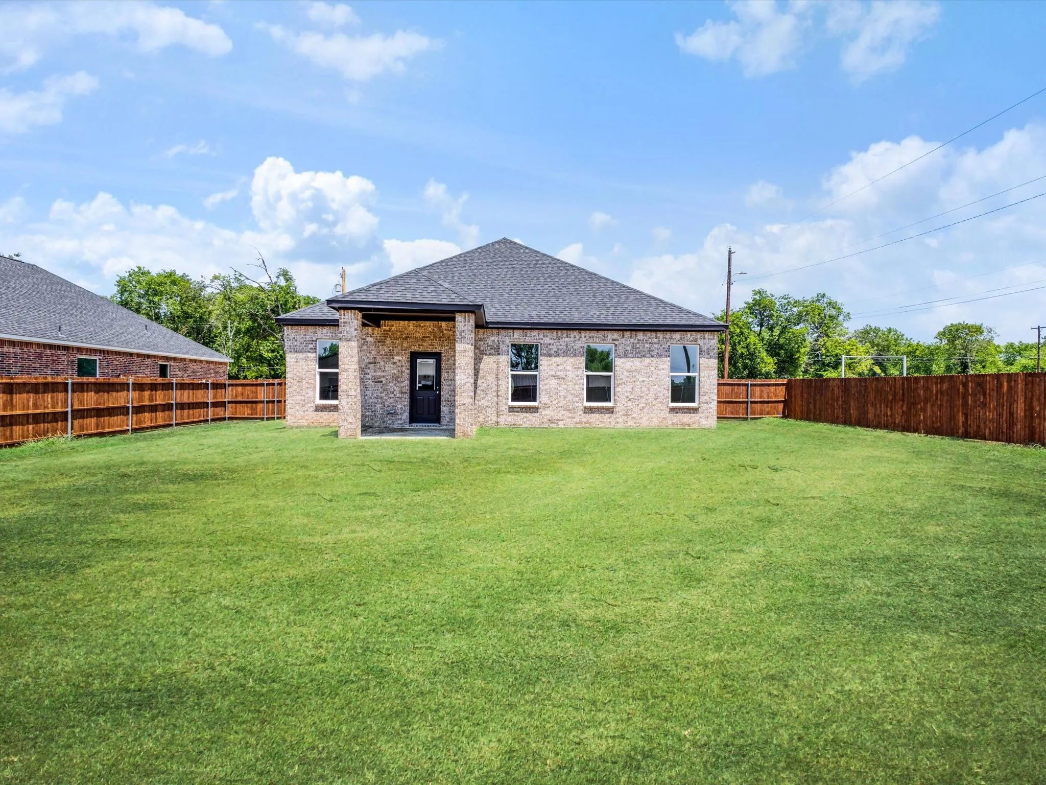 Newly constructed residence with a brick exterior, dark-toned roof, and a covered back patio