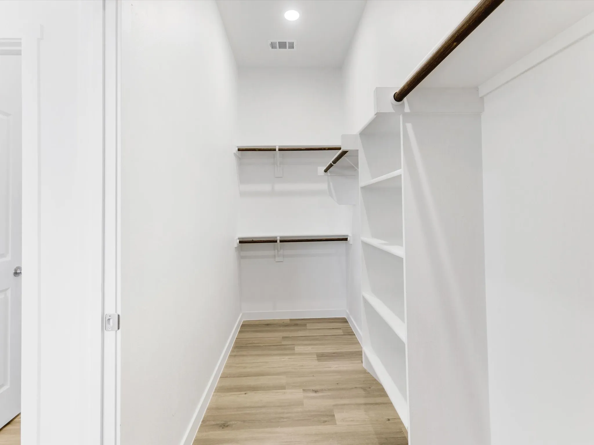 Built-in shelving, hanging rods, recessed lighting, and wood-finish flooring
