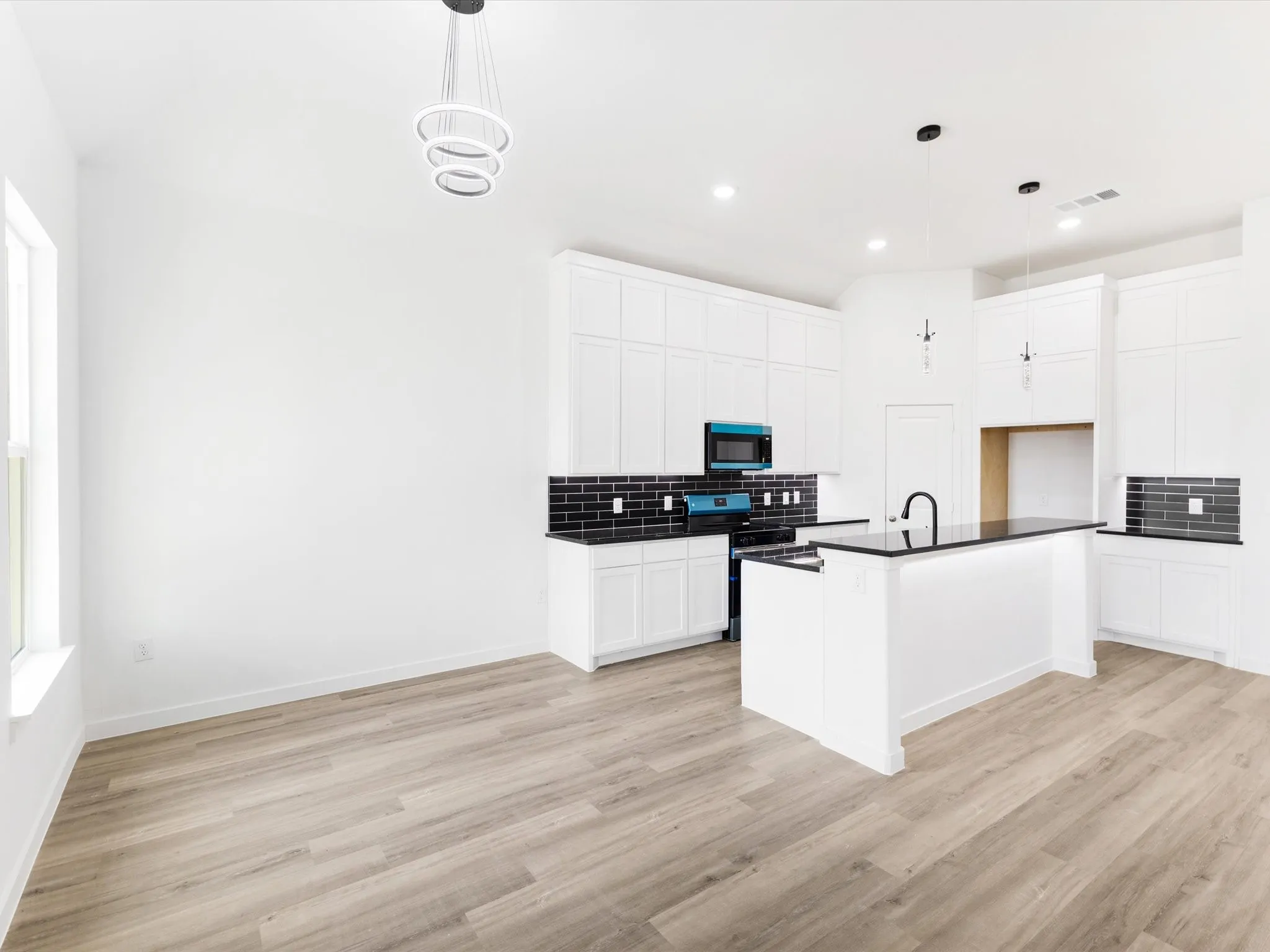 Open-concept kitchen with white cabinetry, black countertops, a central island, and wood-finish flooring
