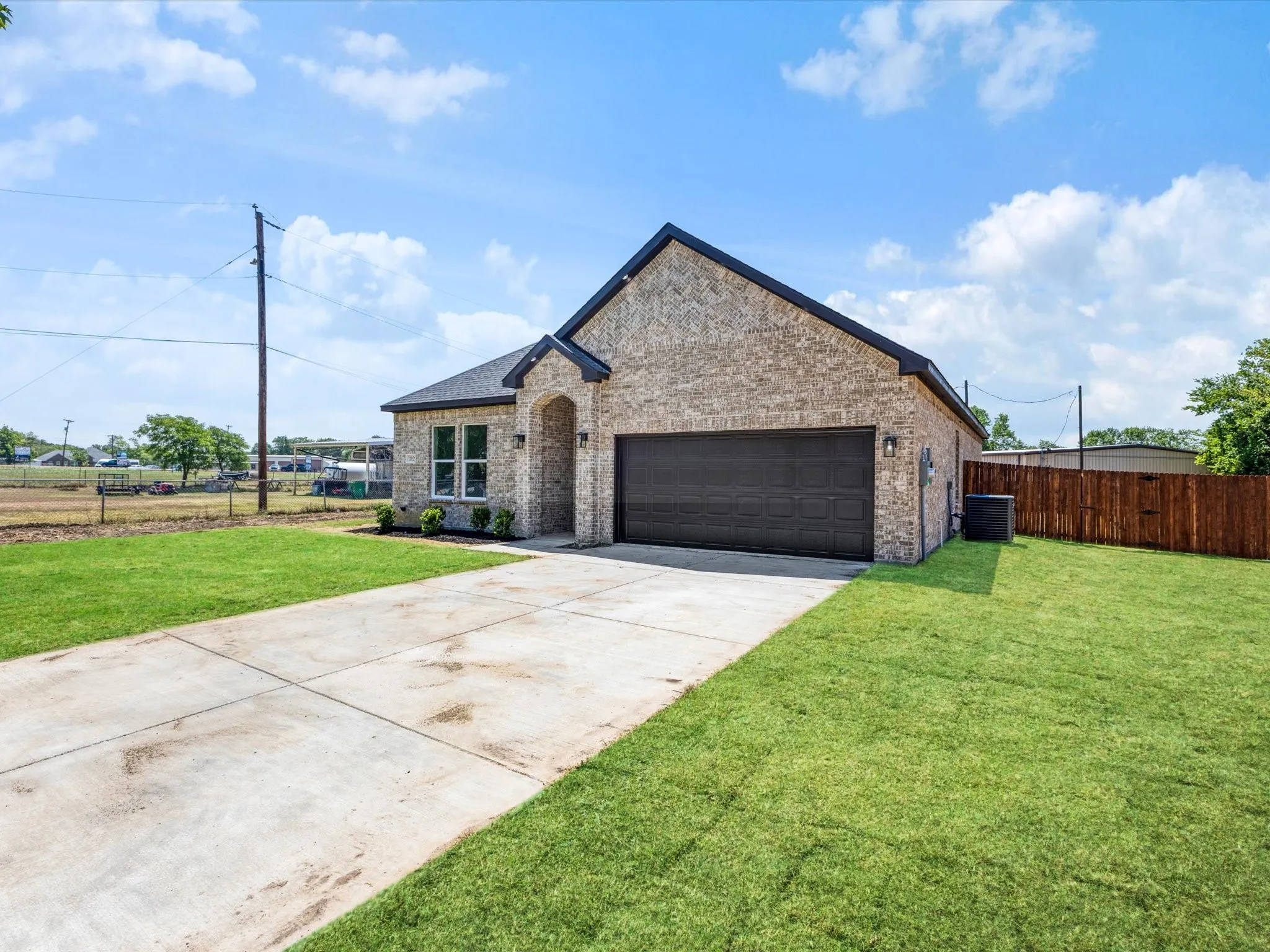 Brick exterior with an arched entry, two-car garage, concrete driveway, and a manicured lawn