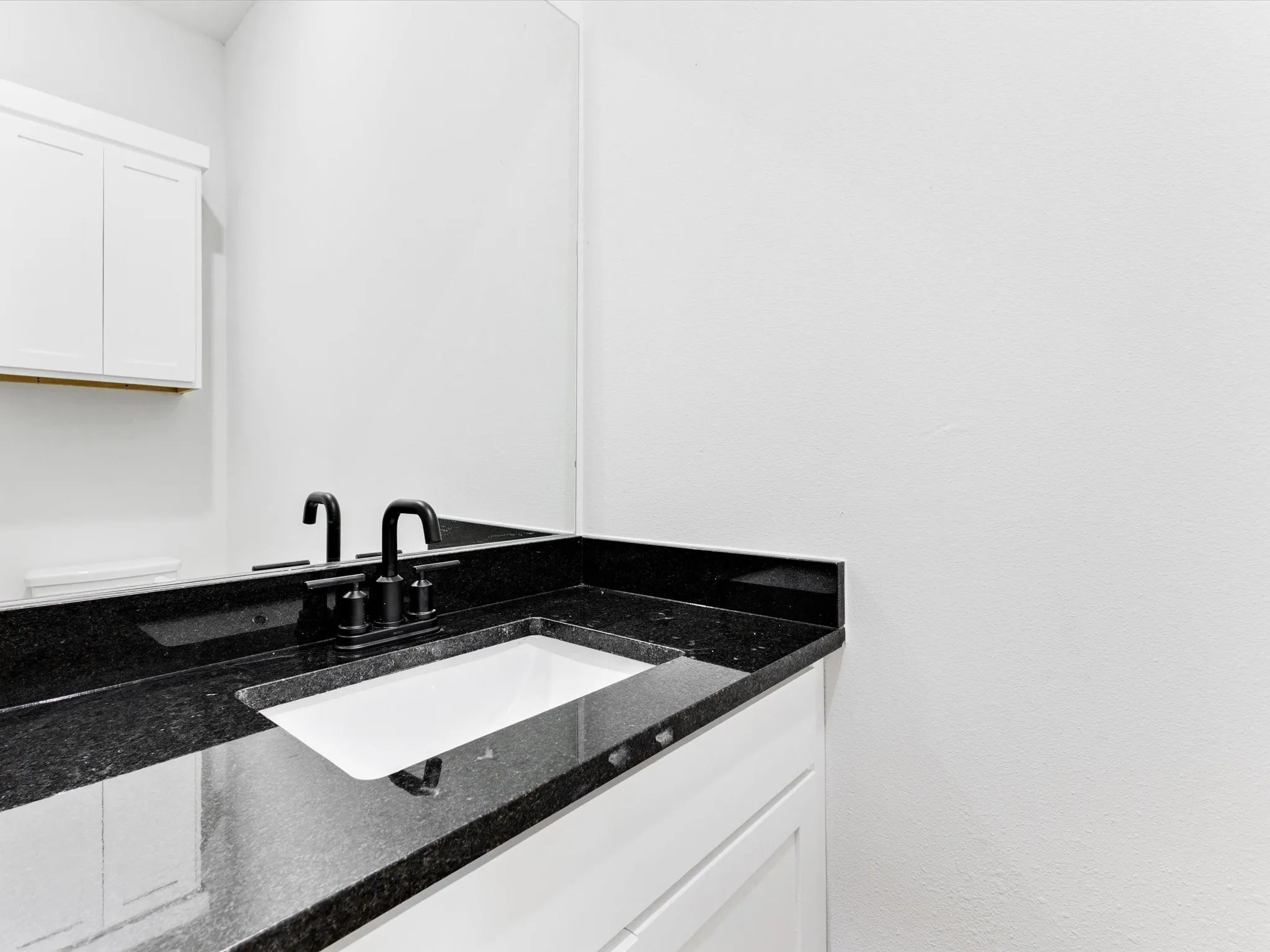 Modern bathroom featuring a black stone countertop with integrated rectangular white vessel sink, matte black wall-mounted faucet, white cabinetry, and clean white tile walls with chrome towel bar
