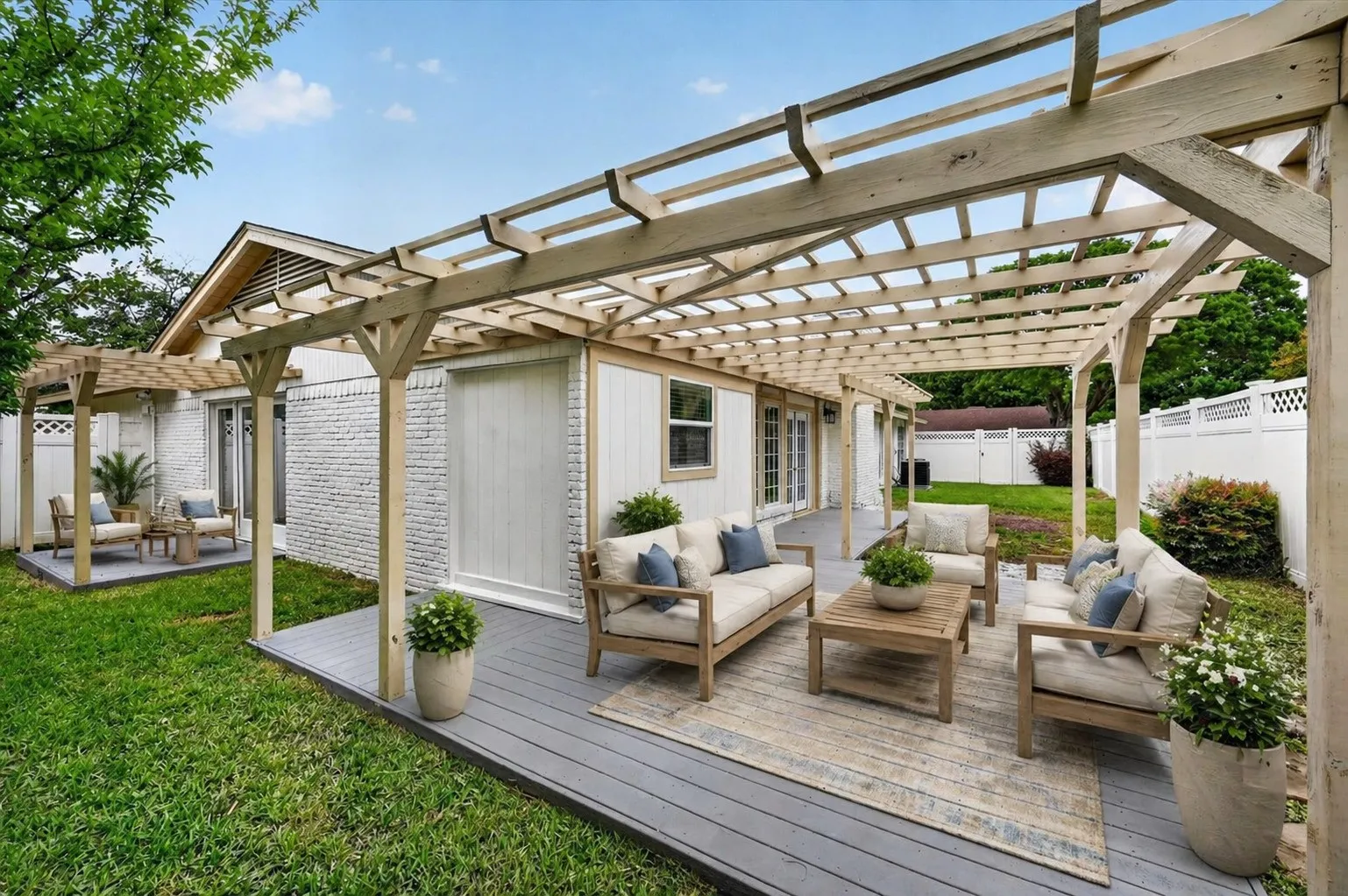 Expansive backyard featuring a large pergola-covered deck, a secondary pergola-covered patio, a white privacy fence, and a manicured lawn