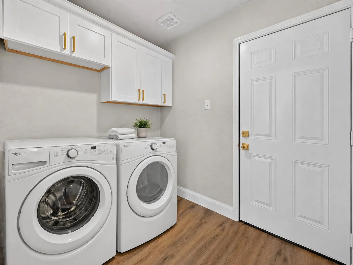 Dedicated laundry area featuring white shaker-style cabinetry with gold-finish hardware, wood-finish flooring, and a paneled entry door with gold-finish hardware