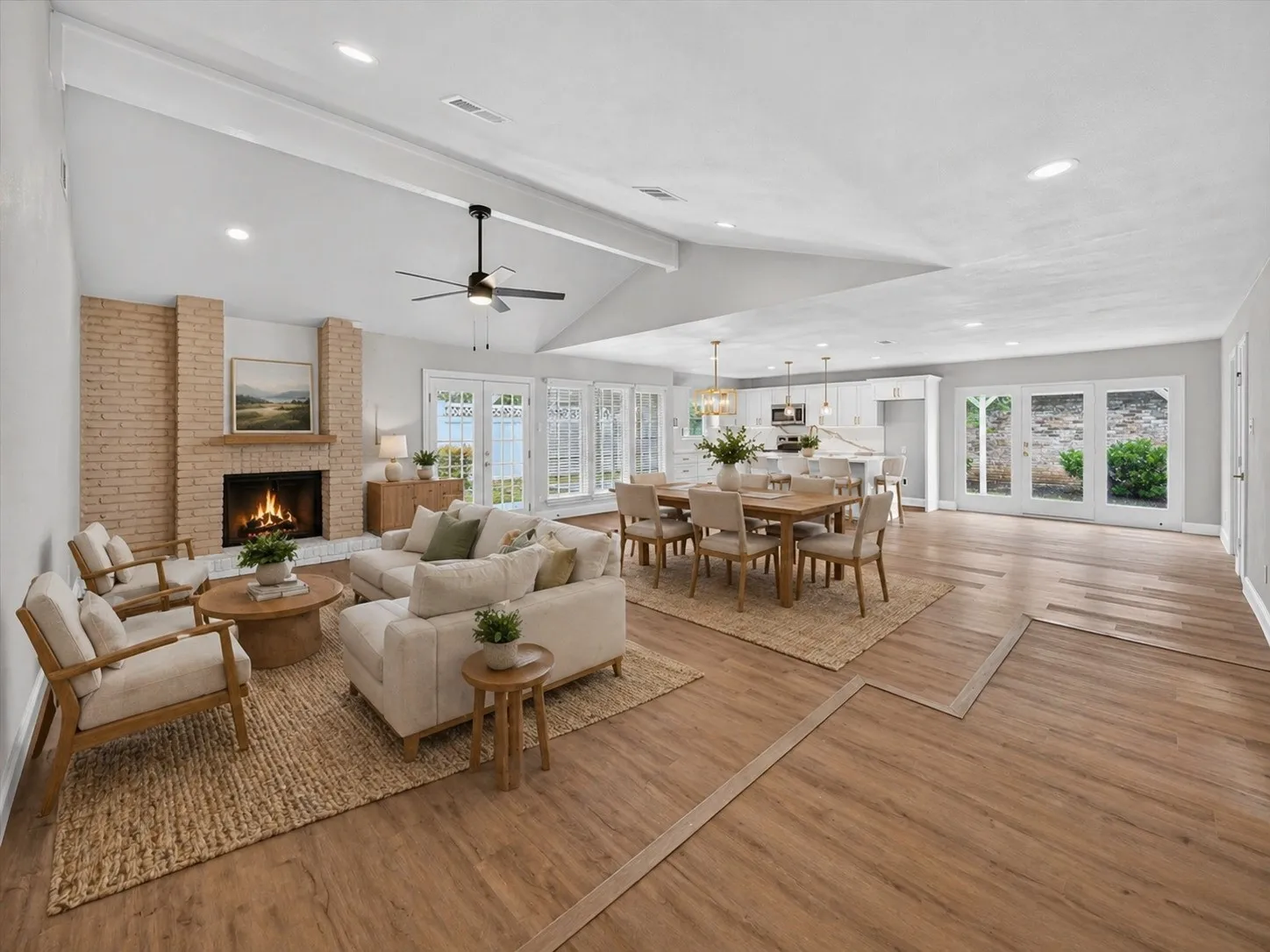 Open-concept living space featuring vaulted ceilings, wood-finish flooring, a brick fireplace with a wood mantle, multiple French doors, and recessed lighting AI generated