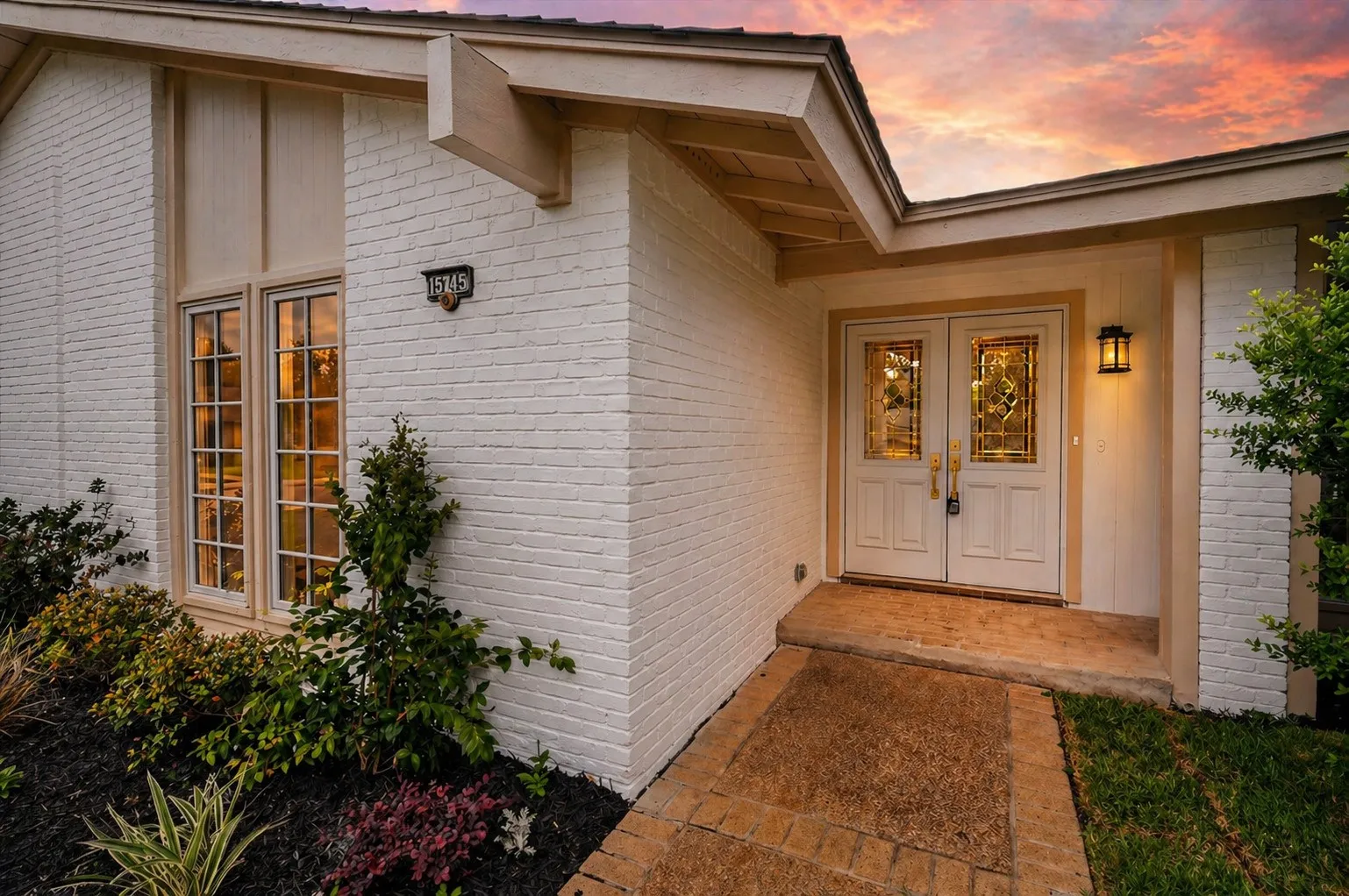 White brick exterior featuring a double-door entry with decorative glass inserts, an exterior wall sconce, and a front window with grilles
