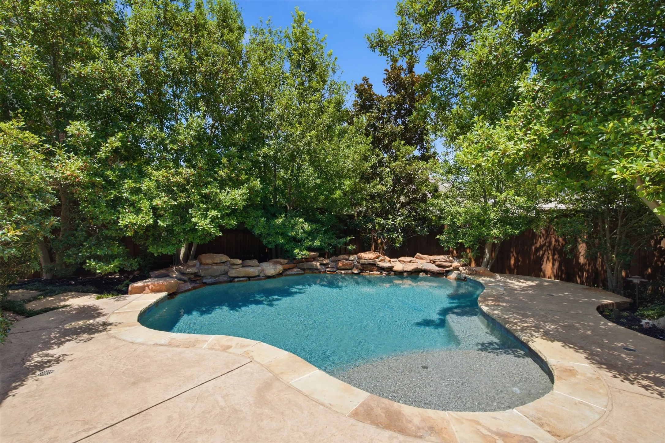 Freeform swimming pool with integrated steps, surrounded by flagstone coping and a natural rock waterfall feature