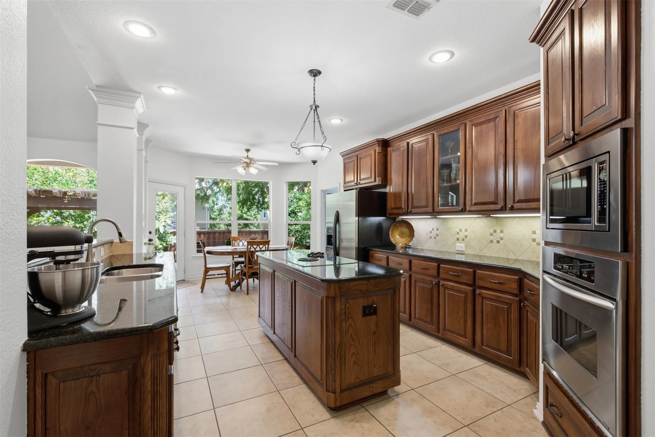 Kitchen featuring wood cabinetry, granite countertops, tile flooring, stainless steel appliances, and a central island with a cooktop