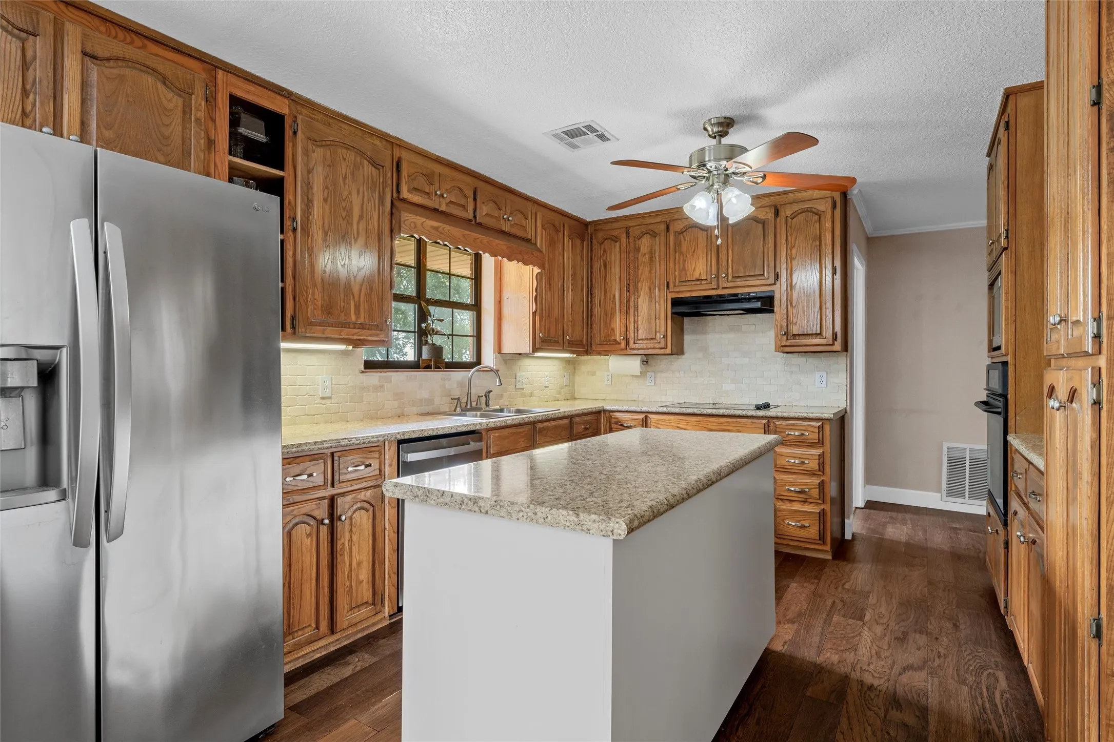 Kitchen featuring an eat-at island with a light-toned countertop, wood-finish flooring, recessed lighting, wood cabinetry, and a tile backsplash
