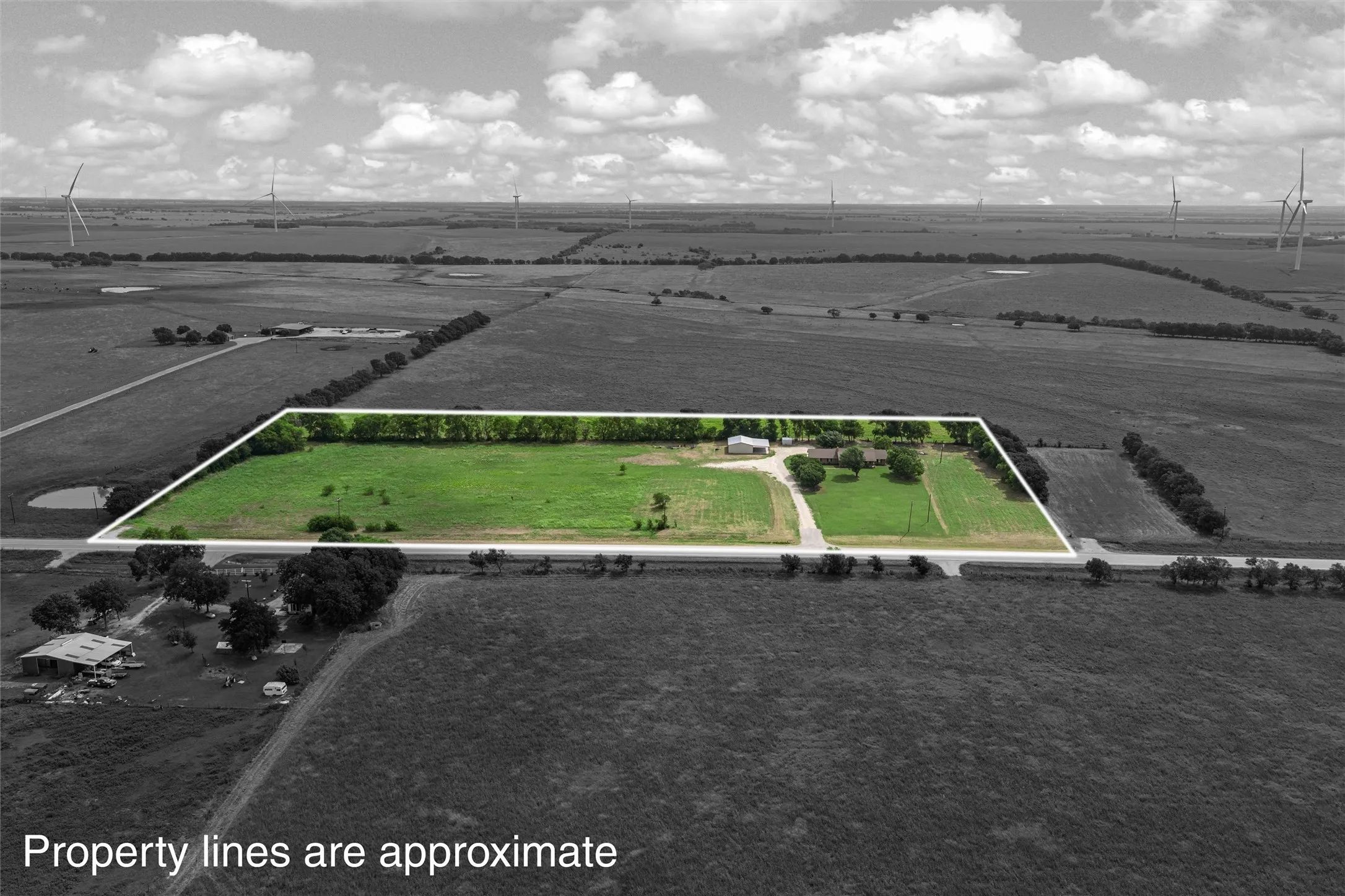 Expansive rural property featuring a large green pasture, mature trees, an outbuilding, and direct road access