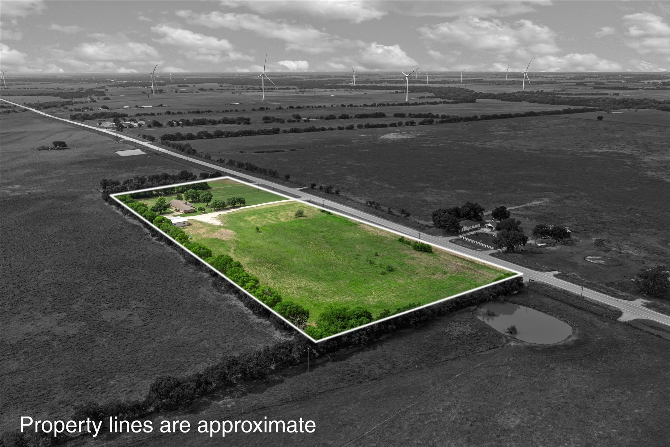 Expansive land parcel featuring open green fields, a residential structure, and a perimeter of mature trees