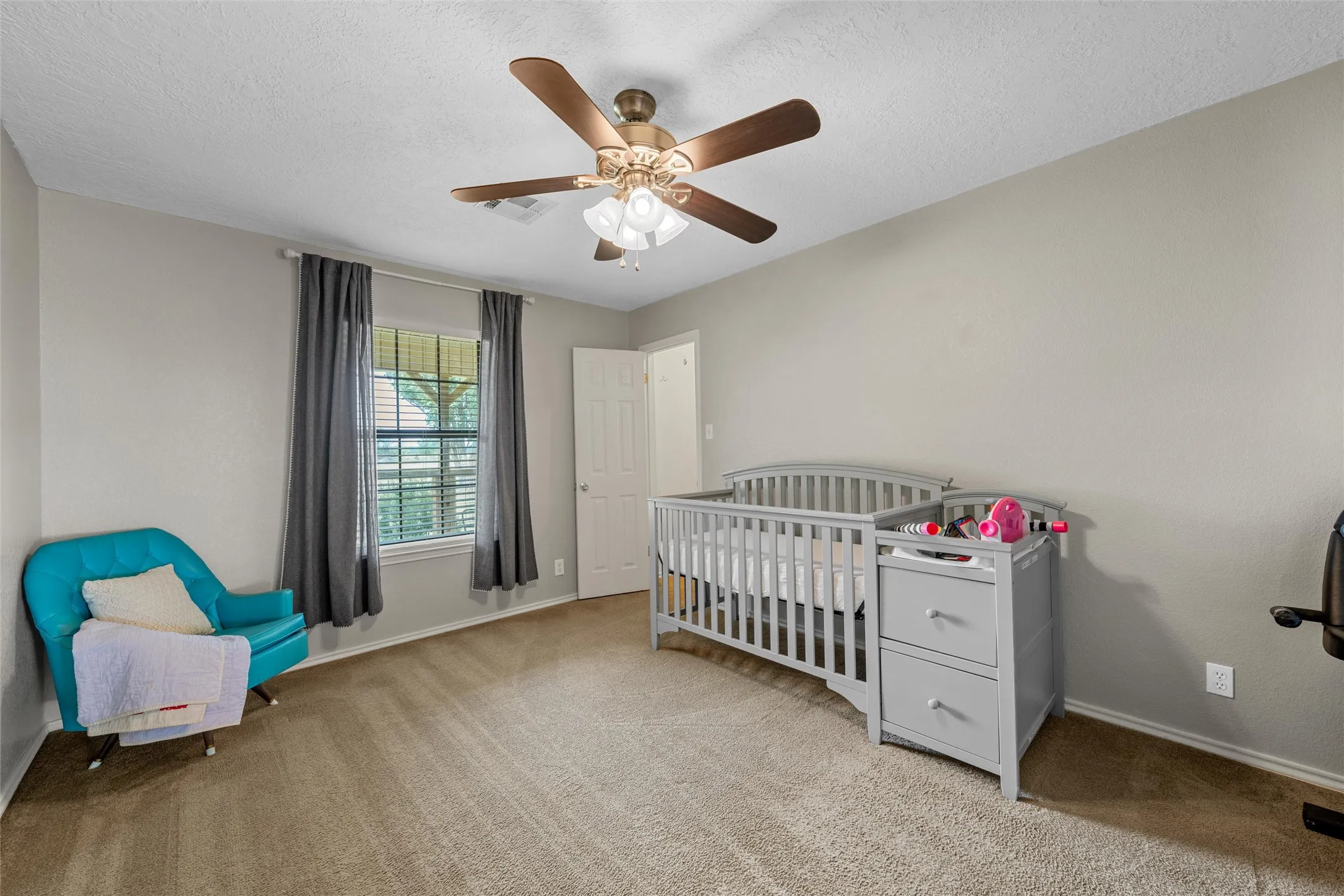 Carpeted room featuring a ceiling fan with light fixture, window with blinds, and a paneled interior door
