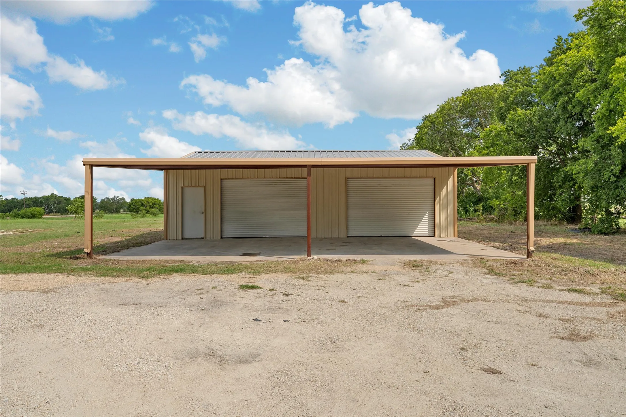Detached metal building featuring two roll-up garage doors, a pedestrian entry door, and an extended carport