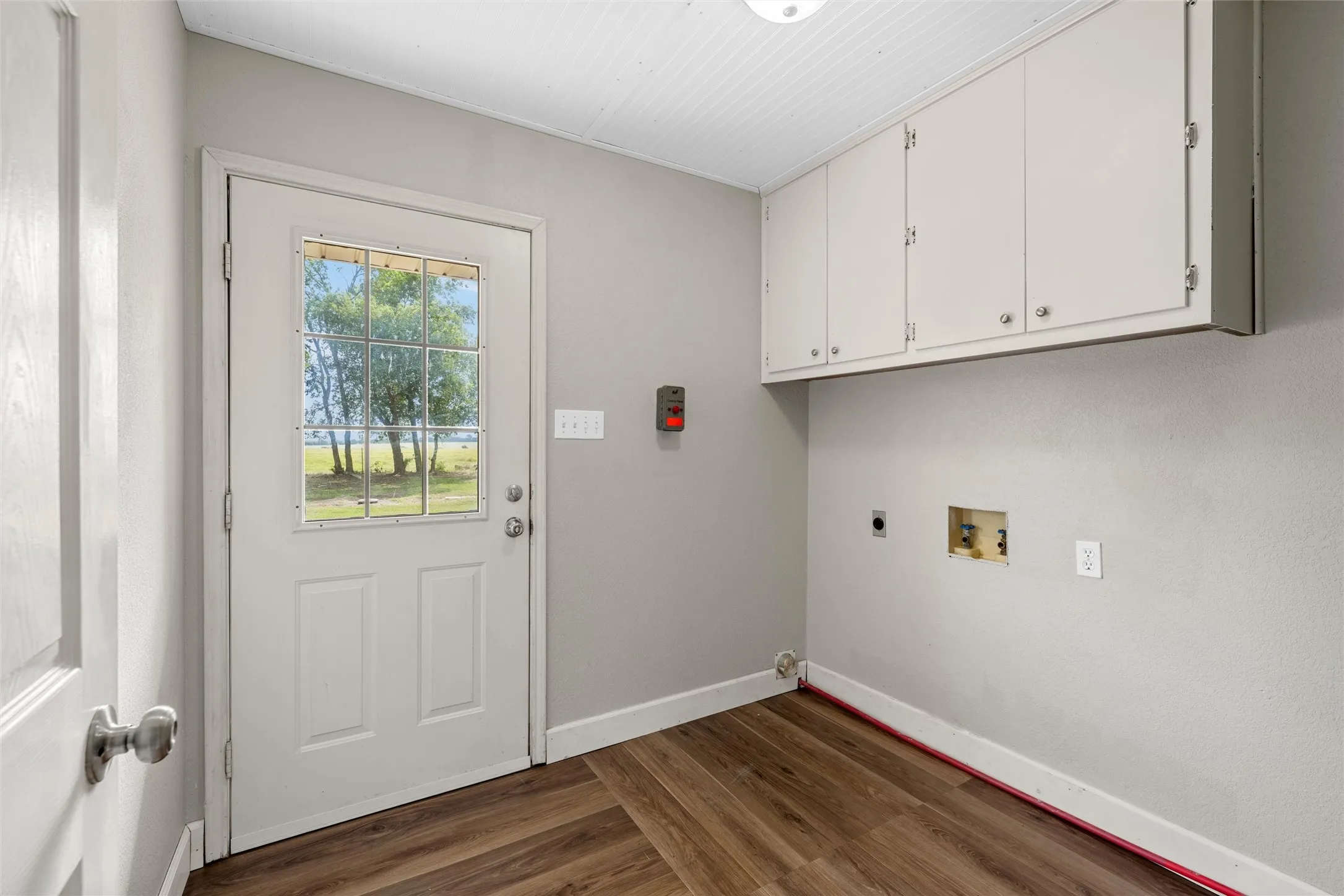 White paneled door with grid window, wood-finish flooring, overhead cabinetry, and beadboard ceiling