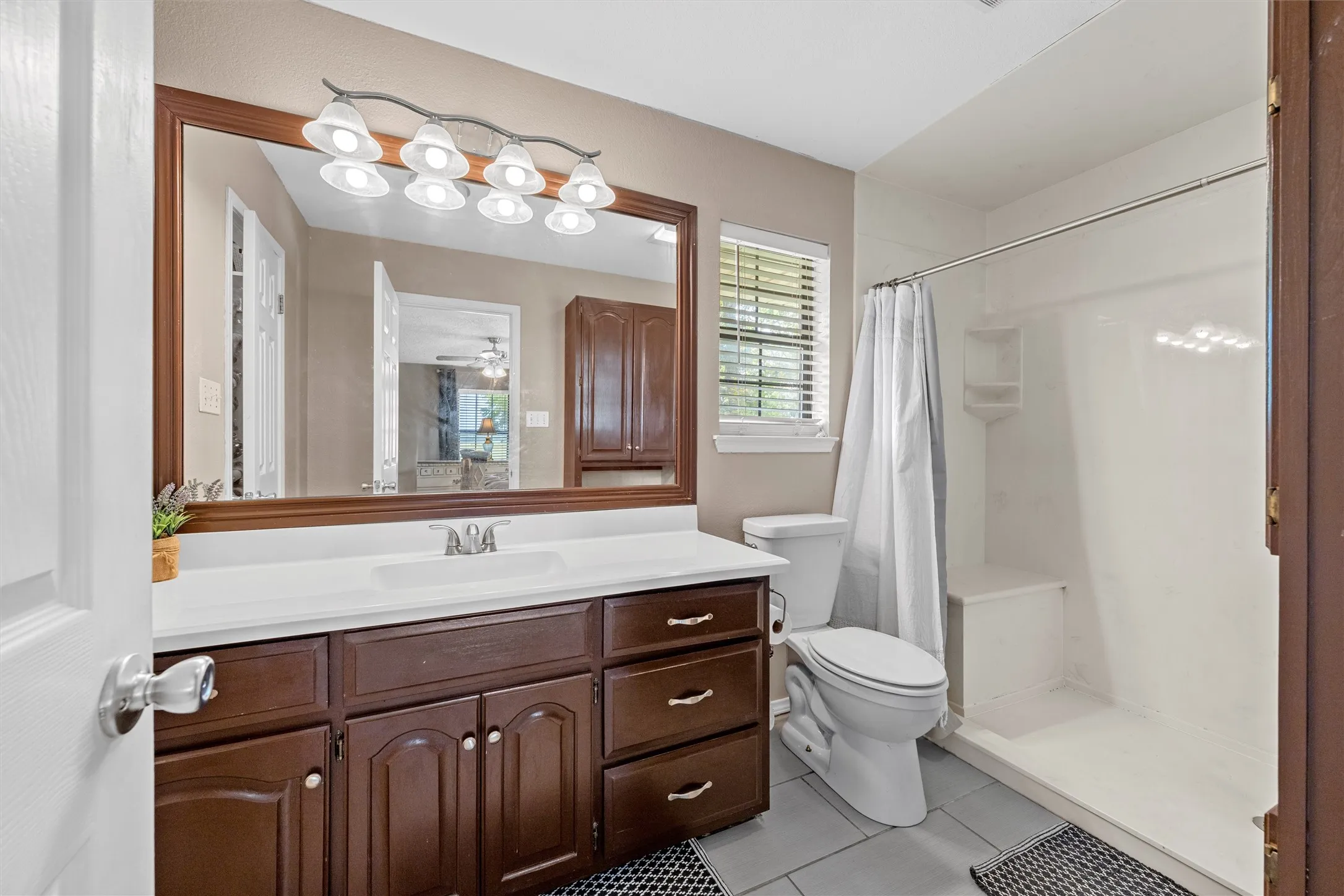 Bathroom featuring a dark wood-finish vanity with a white countertop and undermount sink, a large framed mirror, and a wall-mounted light fixture