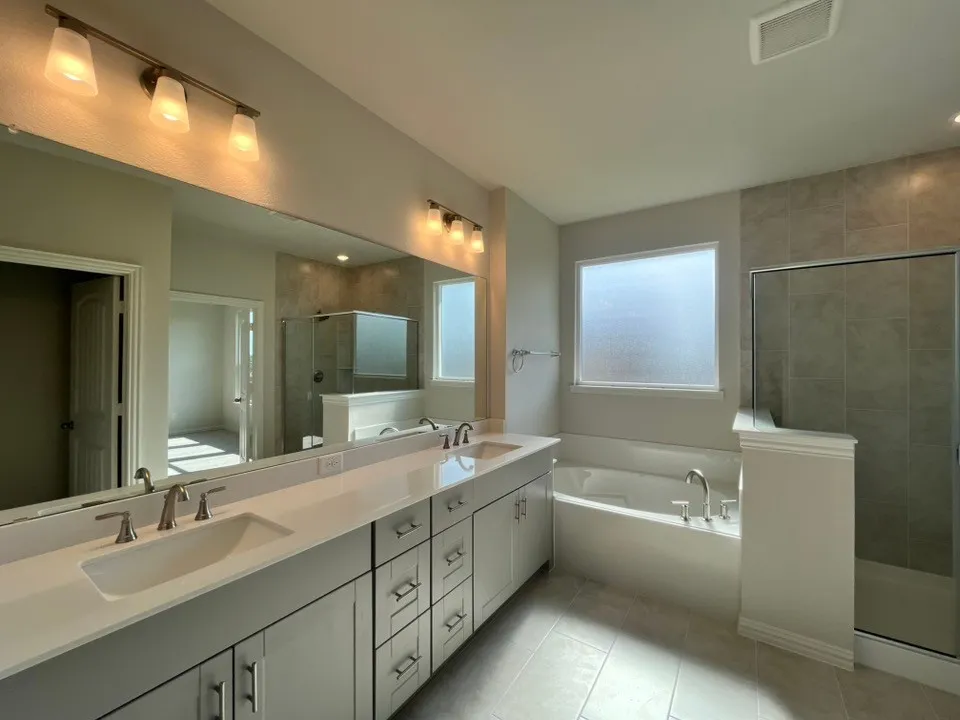 Dual vanity with integrated sinks, contemporary light fixtures, framed glass shower enclosure, and a built-in bathtub