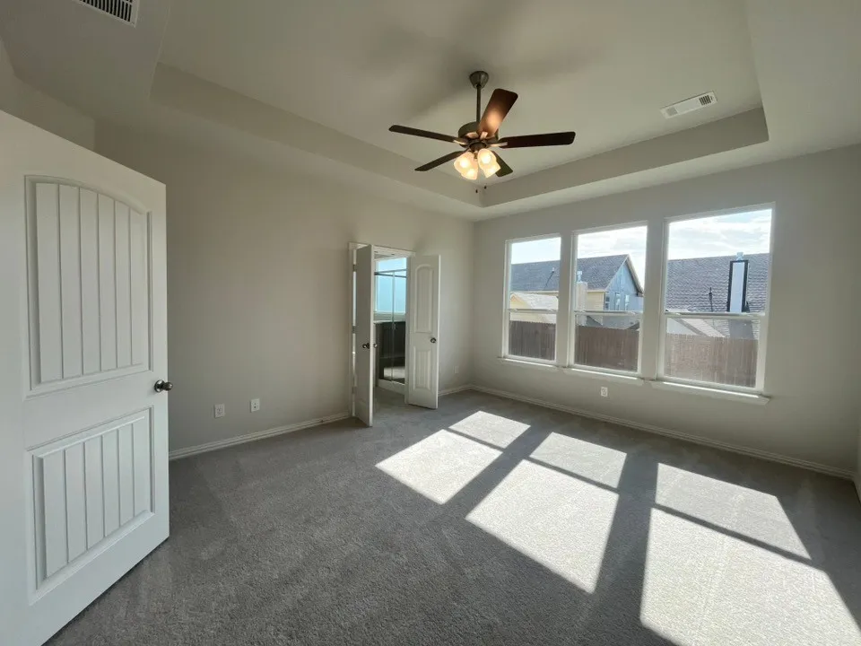 Tray ceiling with a ceiling fan, three large windows, and gray carpeting