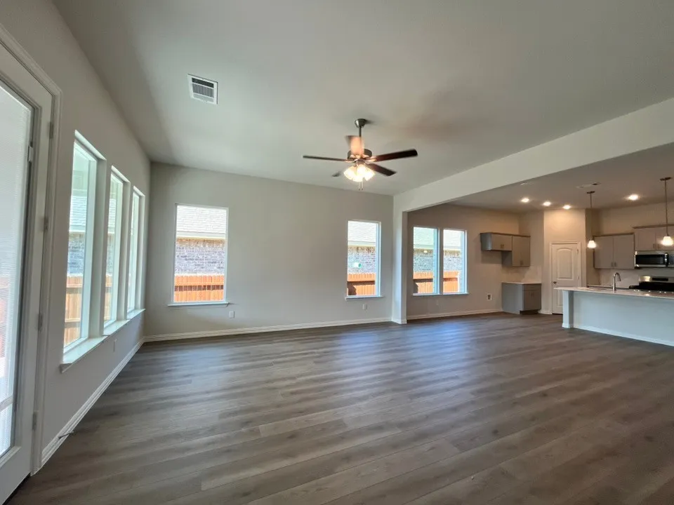 Open-concept living area featuring wood-finish flooring, a ceiling fan, and multiple windows