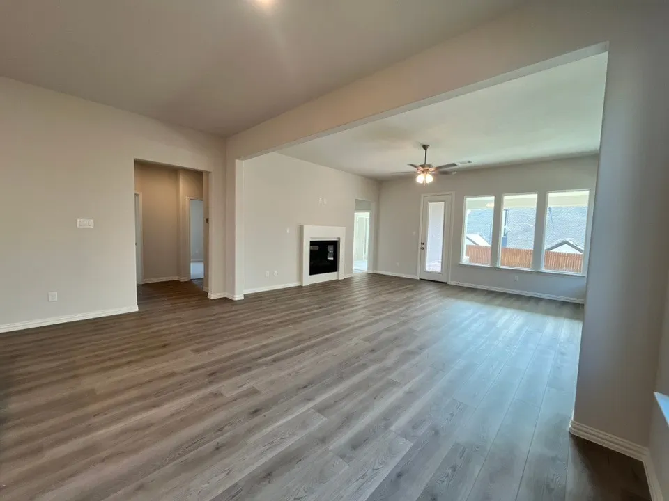 Expansive living area with wood-finish flooring, a white fireplace with a dark insert, a ceiling fan, and multiple large windows