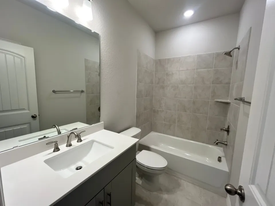 Bathroom featuring a white vanity with an integrated sink, brushed nickel fixtures, a tub/shower combination with tiled surround, and recessed lighting
