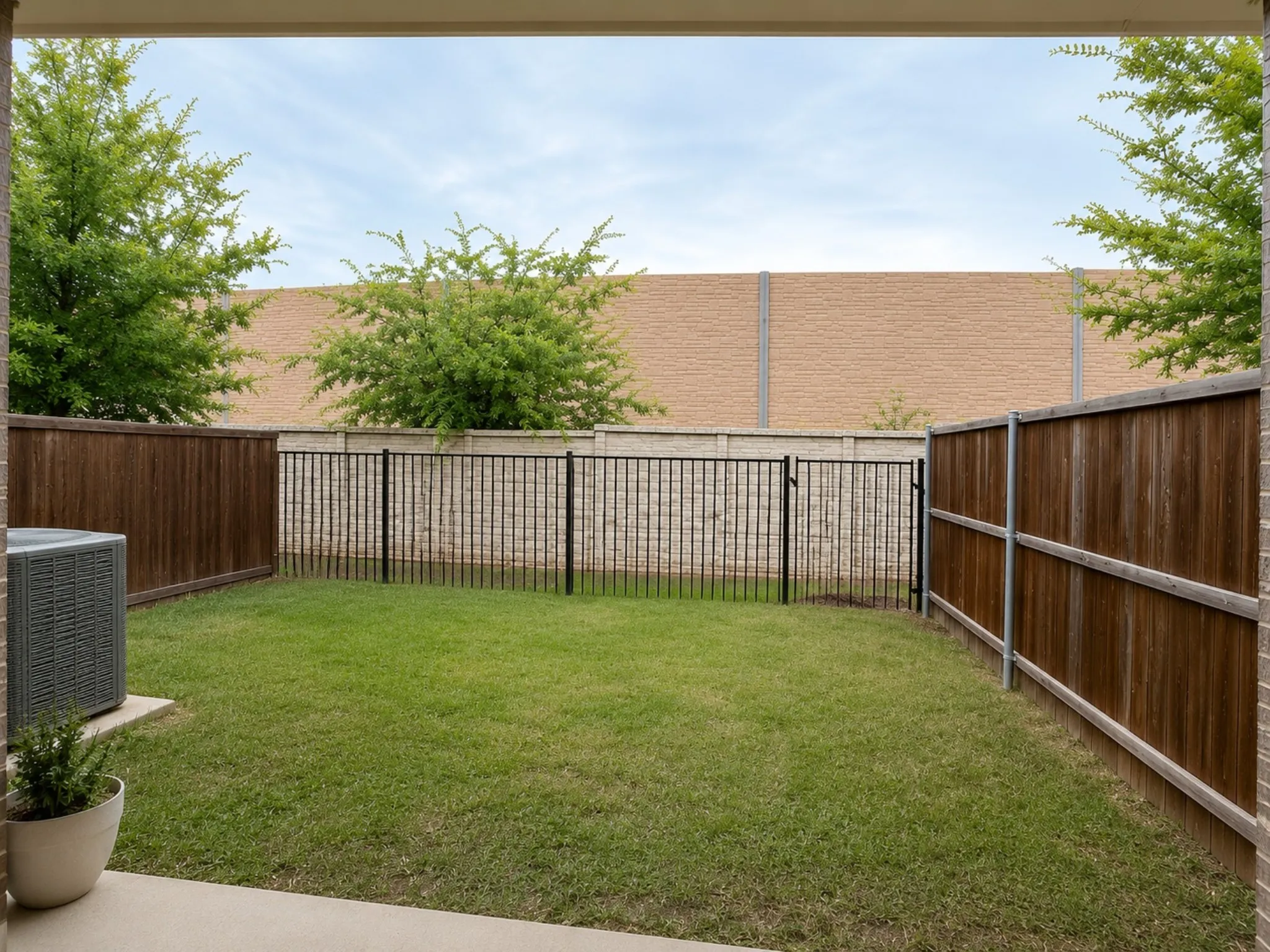 Private outdoor space featuring a manicured lawn, wood fencing, and a black wrought iron fence with gate