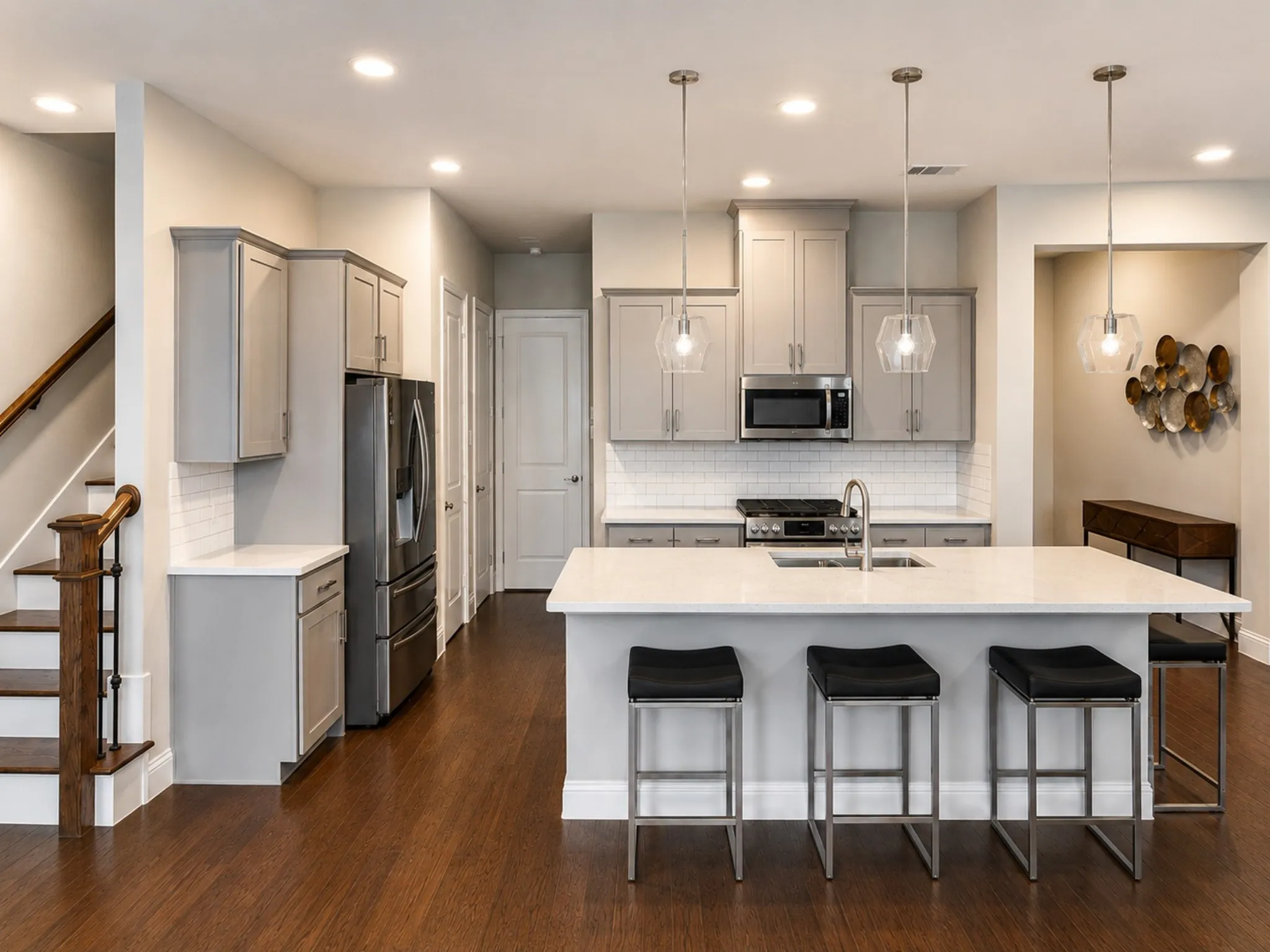 Open-concept kitchen featuring an oversized island with seating, stainless steel appliances, light gray cabinetry, and wood-finish flooring