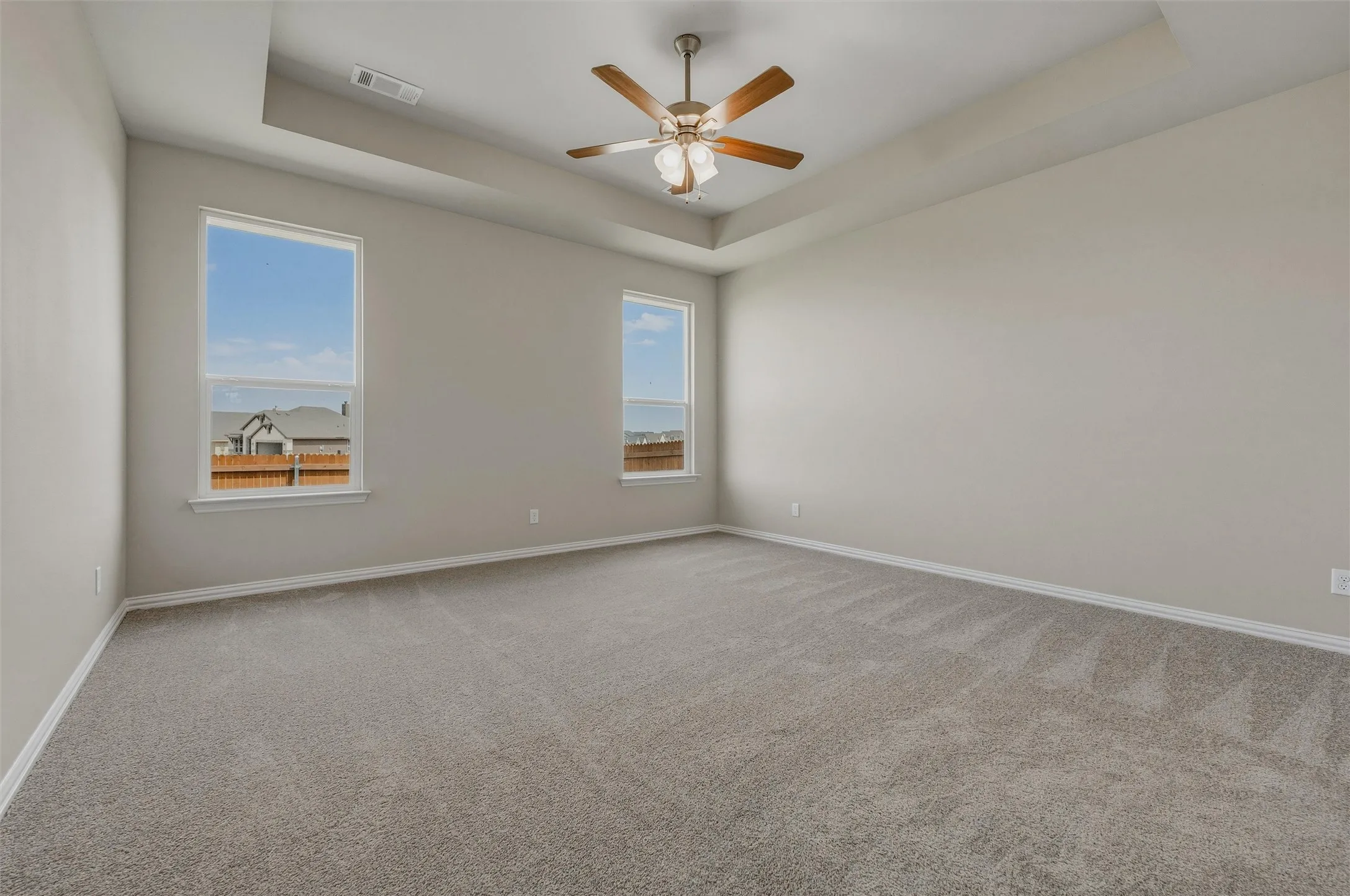 Recessed ceiling with an integrated ceiling fan, two large windows, and neutral carpeting