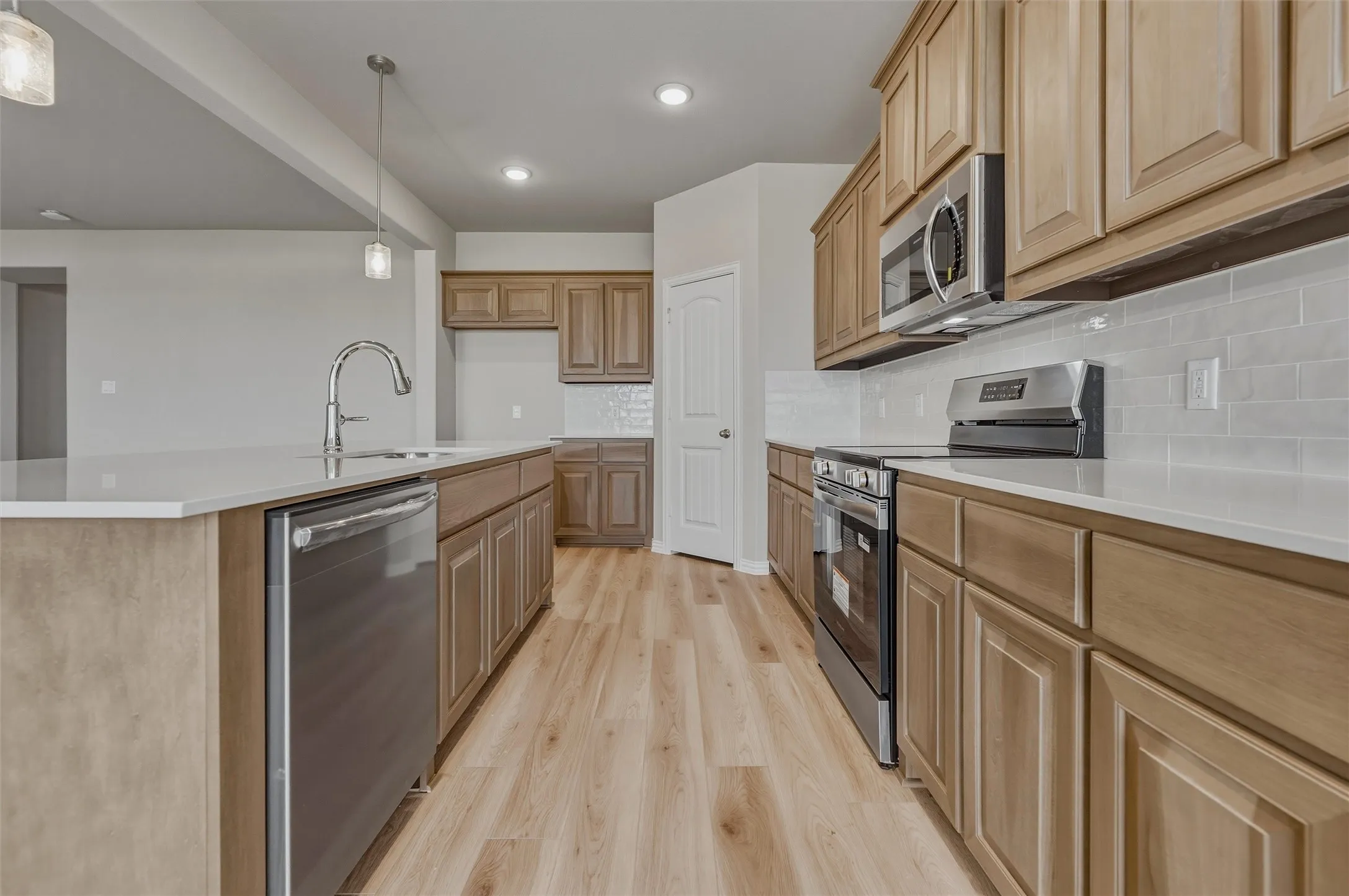 Kitchen featuring wood-finish cabinetry, stainless steel appliances, light-toned countertops, subway tile backsplash, and wood-finish flooring