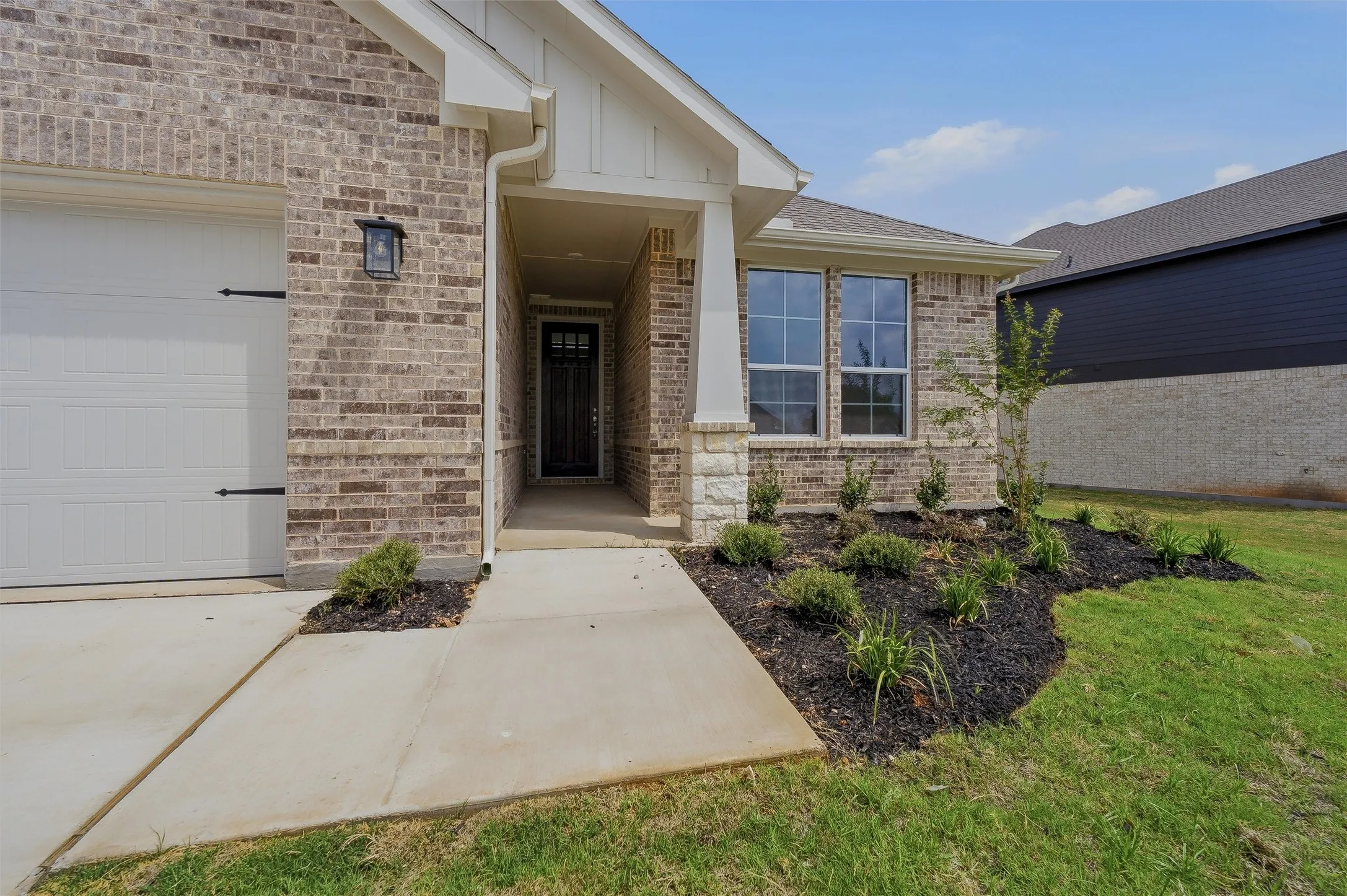 Brick exterior with stone accents, covered front entry, attached garage with decorative hardware, and mature landscaping