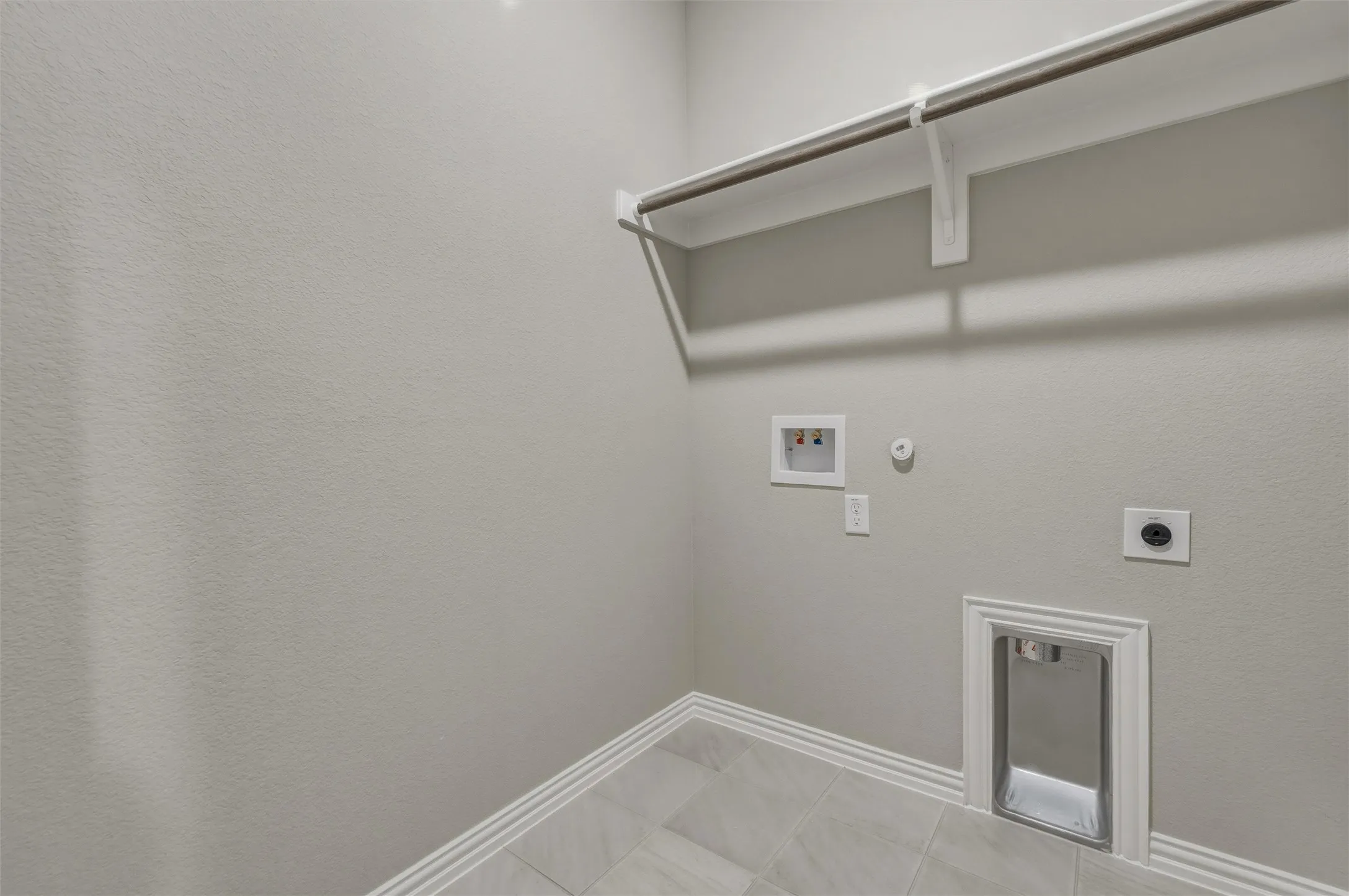Utility connections with a dryer vent, light gray wall paint, and light-toned tile flooring
