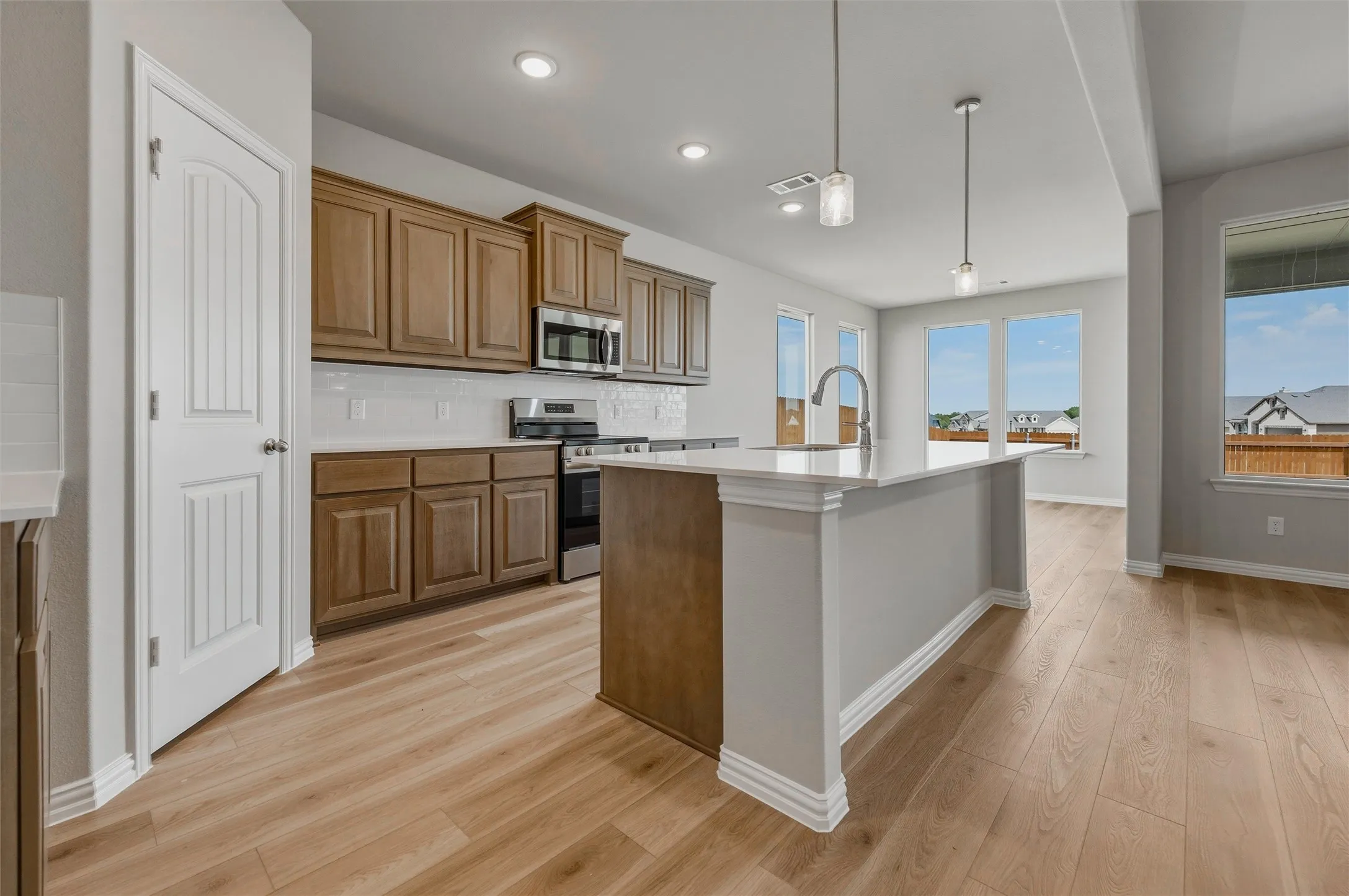 Wood-finish flooring throughout, kitchen island with countertop, stainless steel appliances, recessed lighting, and ample natural light