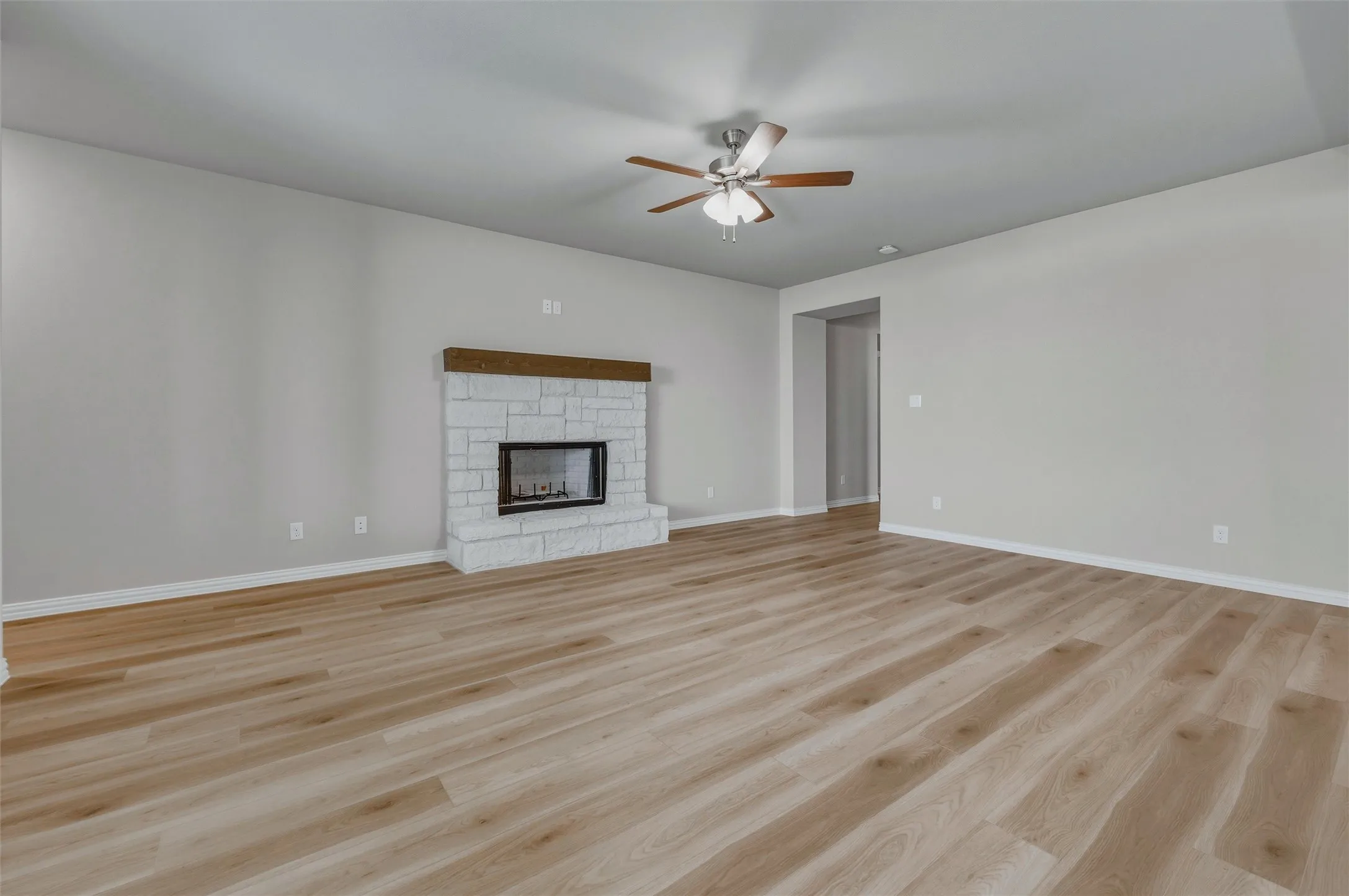Spacious living area featuring wood-finish flooring, a white brick fireplace with a wood mantle, and a ceiling fan