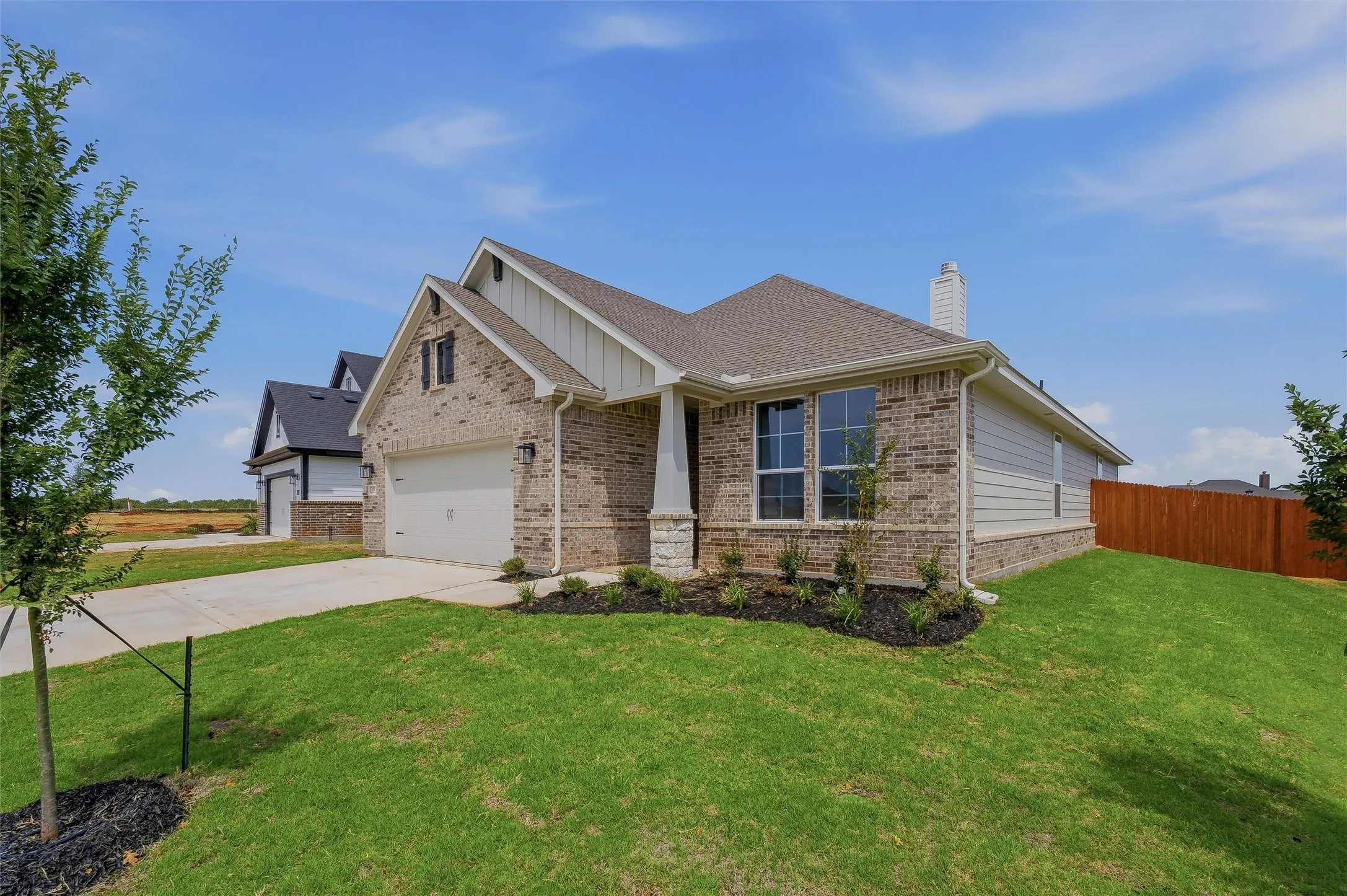Brick exterior with white siding accents, integrated two-car garage, established front landscaping, and a fenced backyard