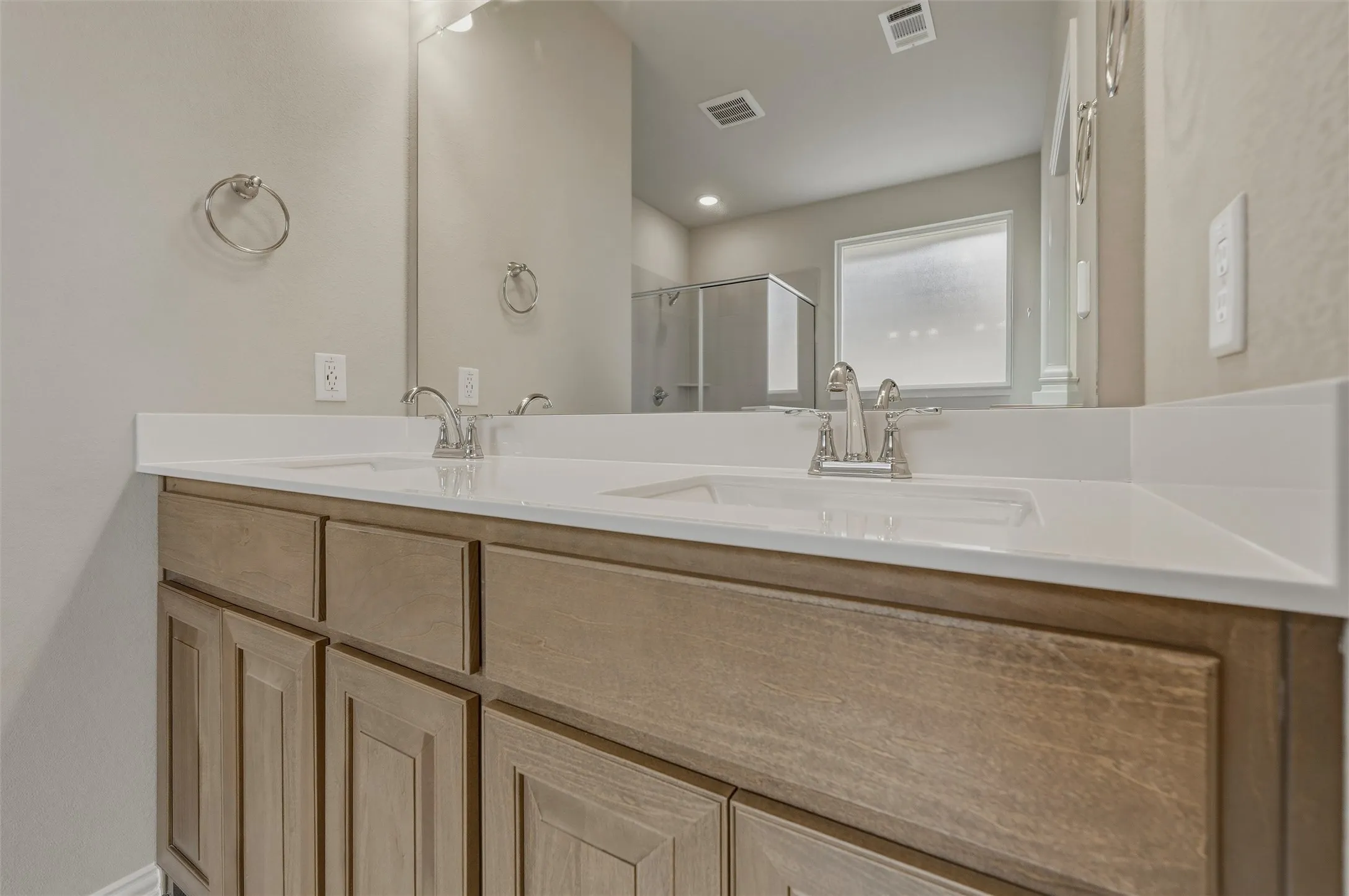 Dual undermount sinks with brushed nickel fixtures, set in a light-colored countertop over wood-finish cabinetry