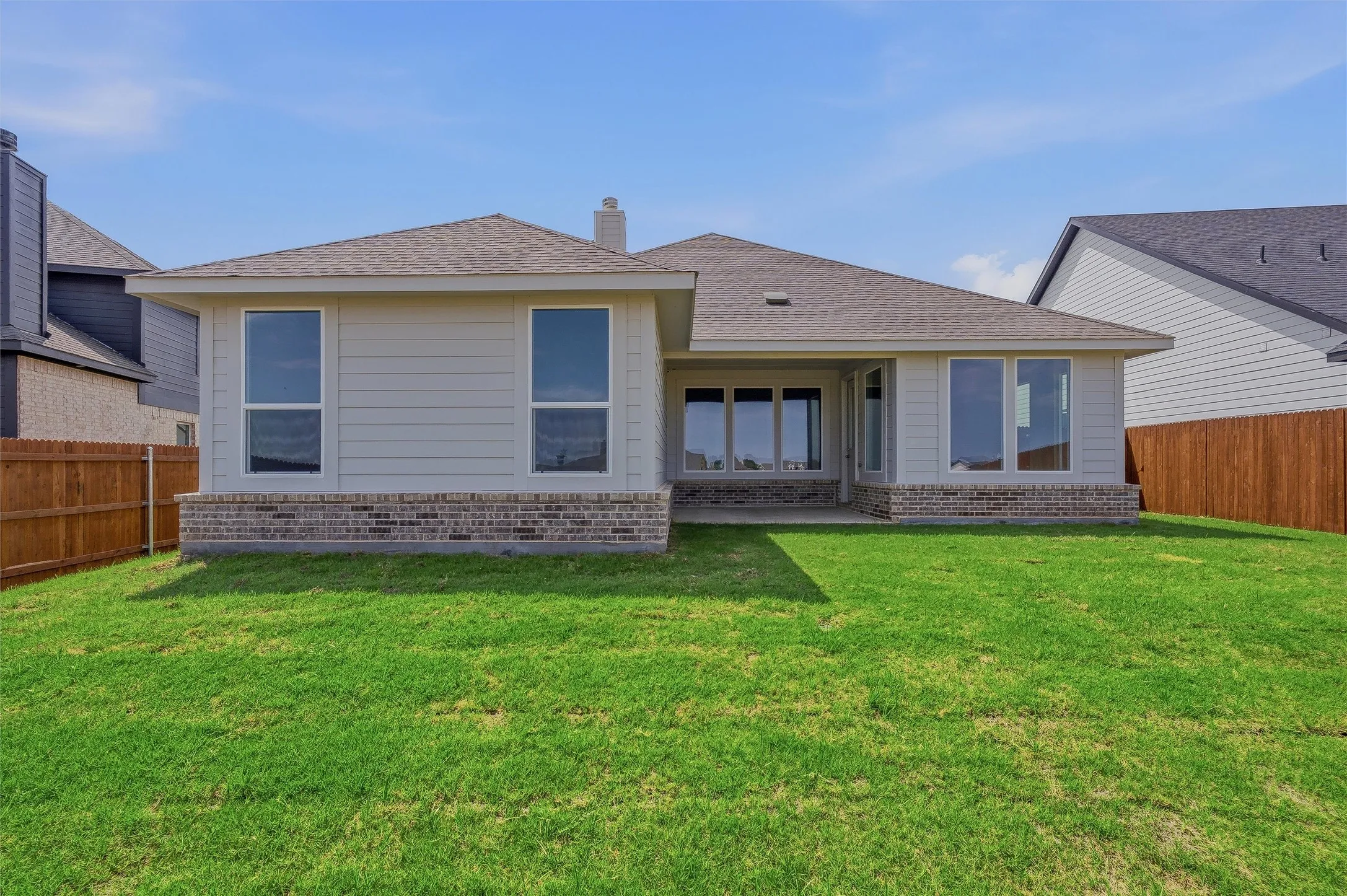 Expansive green lawn with a covered patio, extensive windows, and a brick and siding exterior