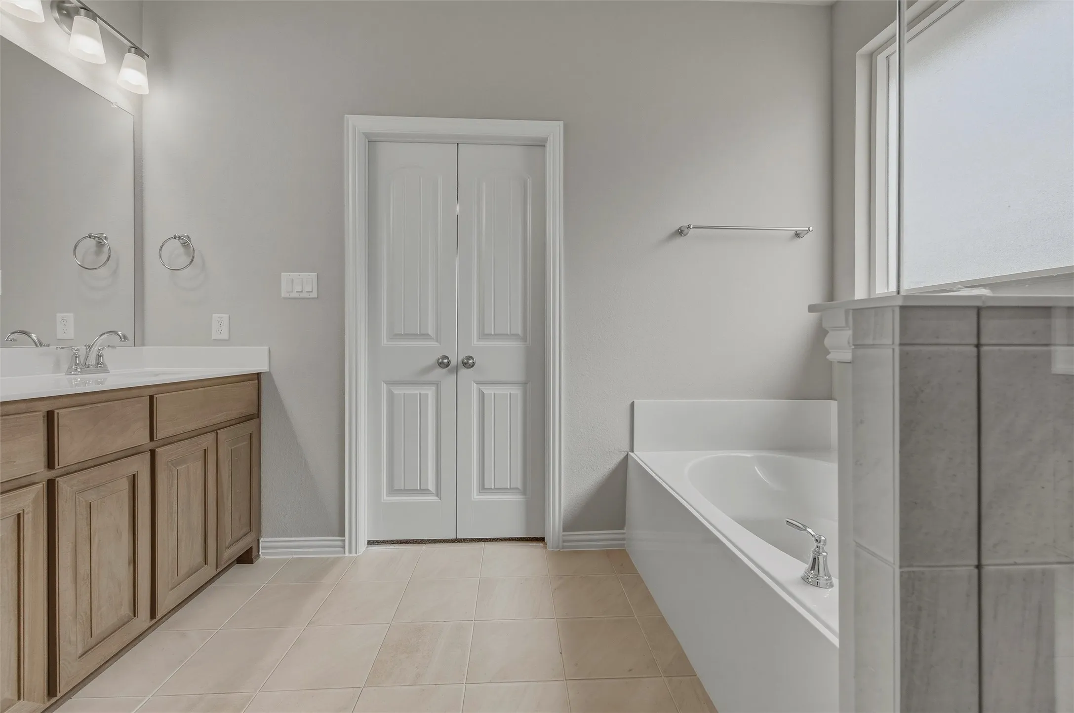 Dual sink vanity with wood-finish cabinetry, tile flooring, built-in bathtub, and a shower with frosted glass