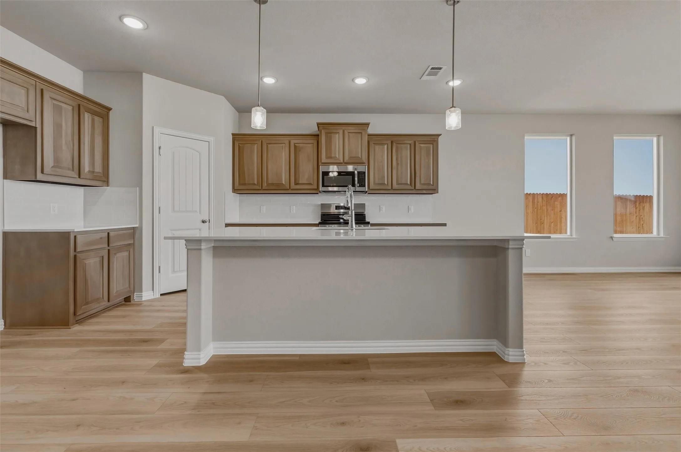 Kitchen featuring wood-finish cabinetry, a large center island with a sink, stainless steel appliances, and a tile backsplash