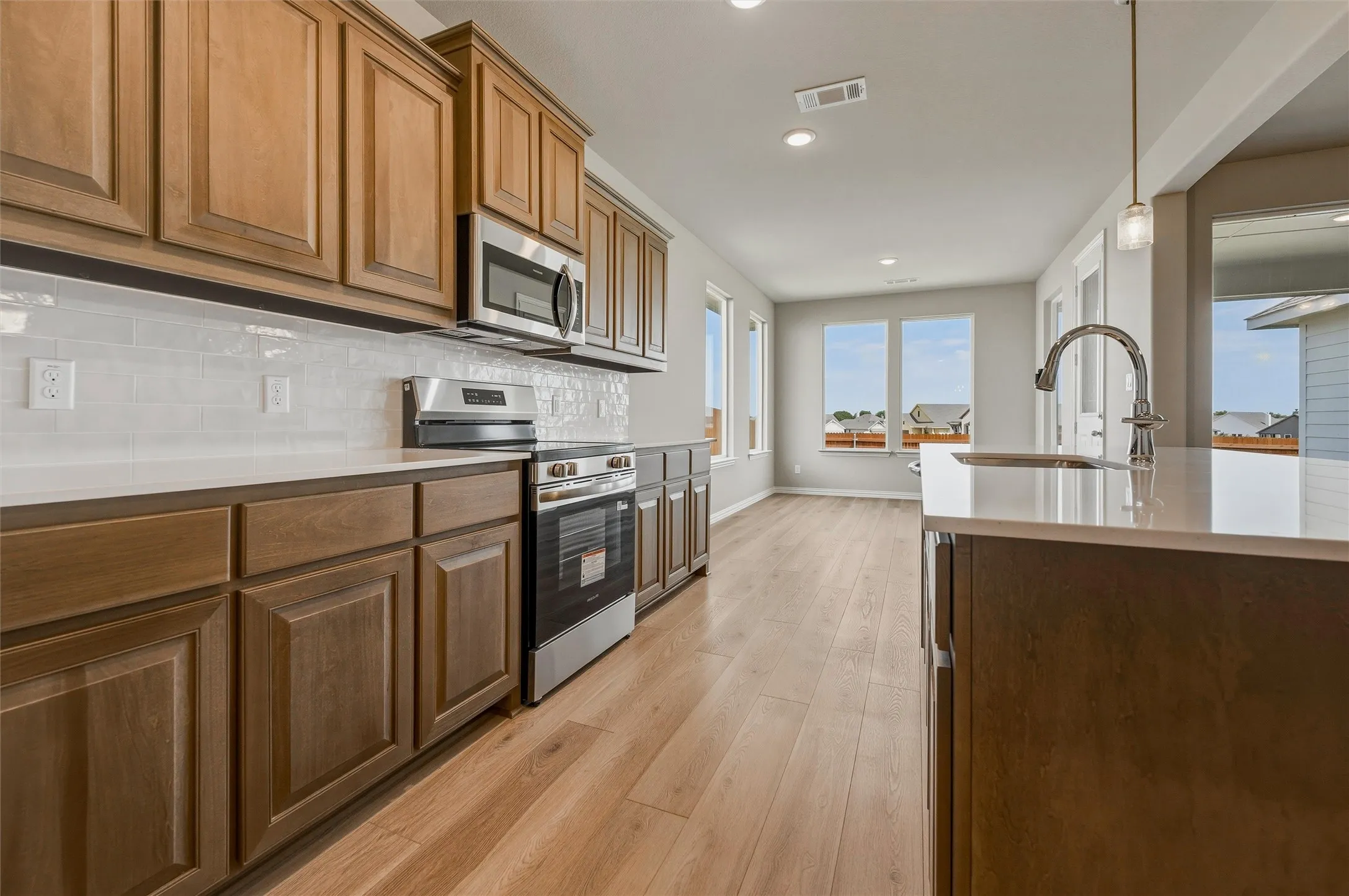 Wood-finish flooring throughout, stainless steel appliances, white subway tile backsplash, recessed lighting, and an island with a gooseneck faucet