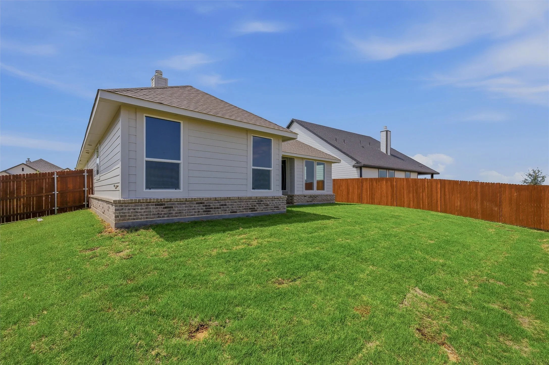 Expansive backyard with a full privacy fence, manicured lawn, and brick and siding exterior