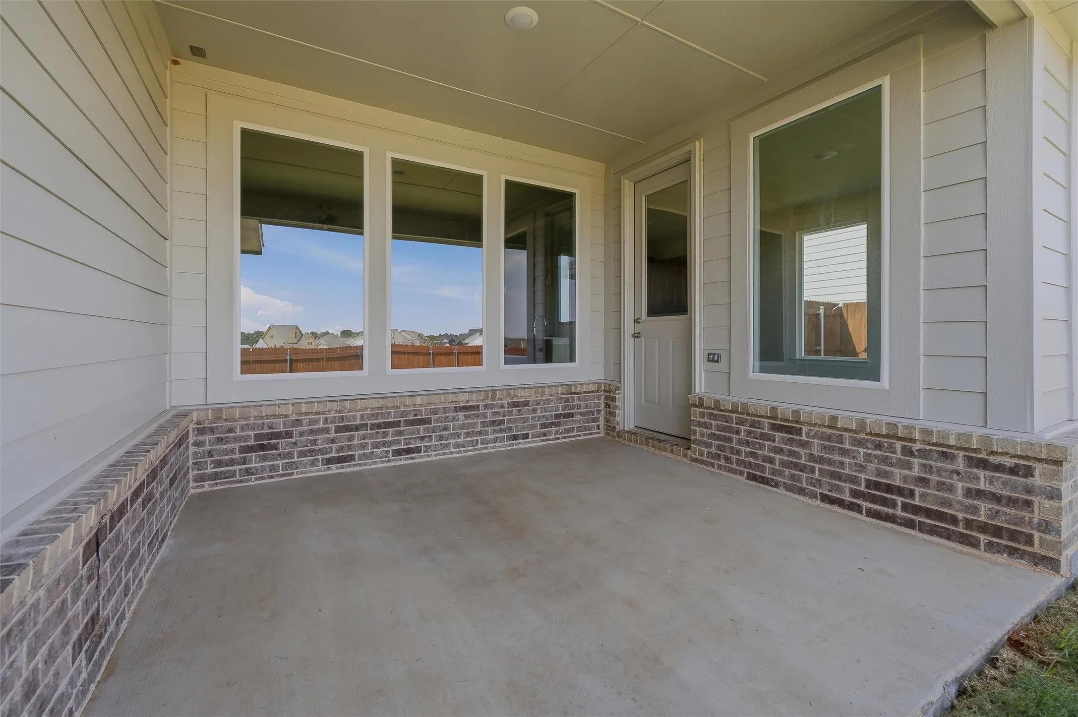 Covered concrete patio with a brick wainscoting and horizontal siding