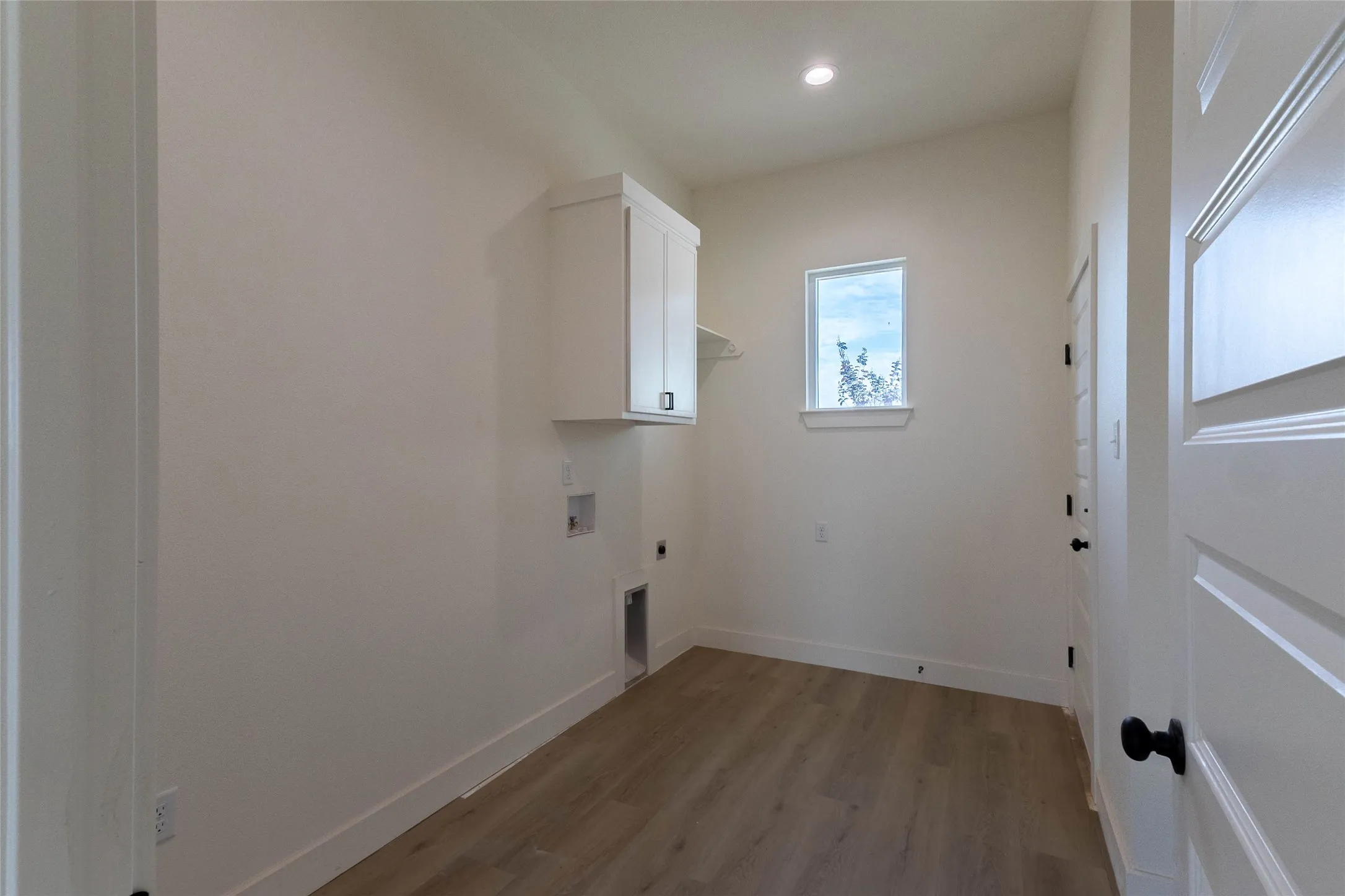 Laundry area featuring wood-finish flooring, white cabinetry, recessed lighting, and a single window