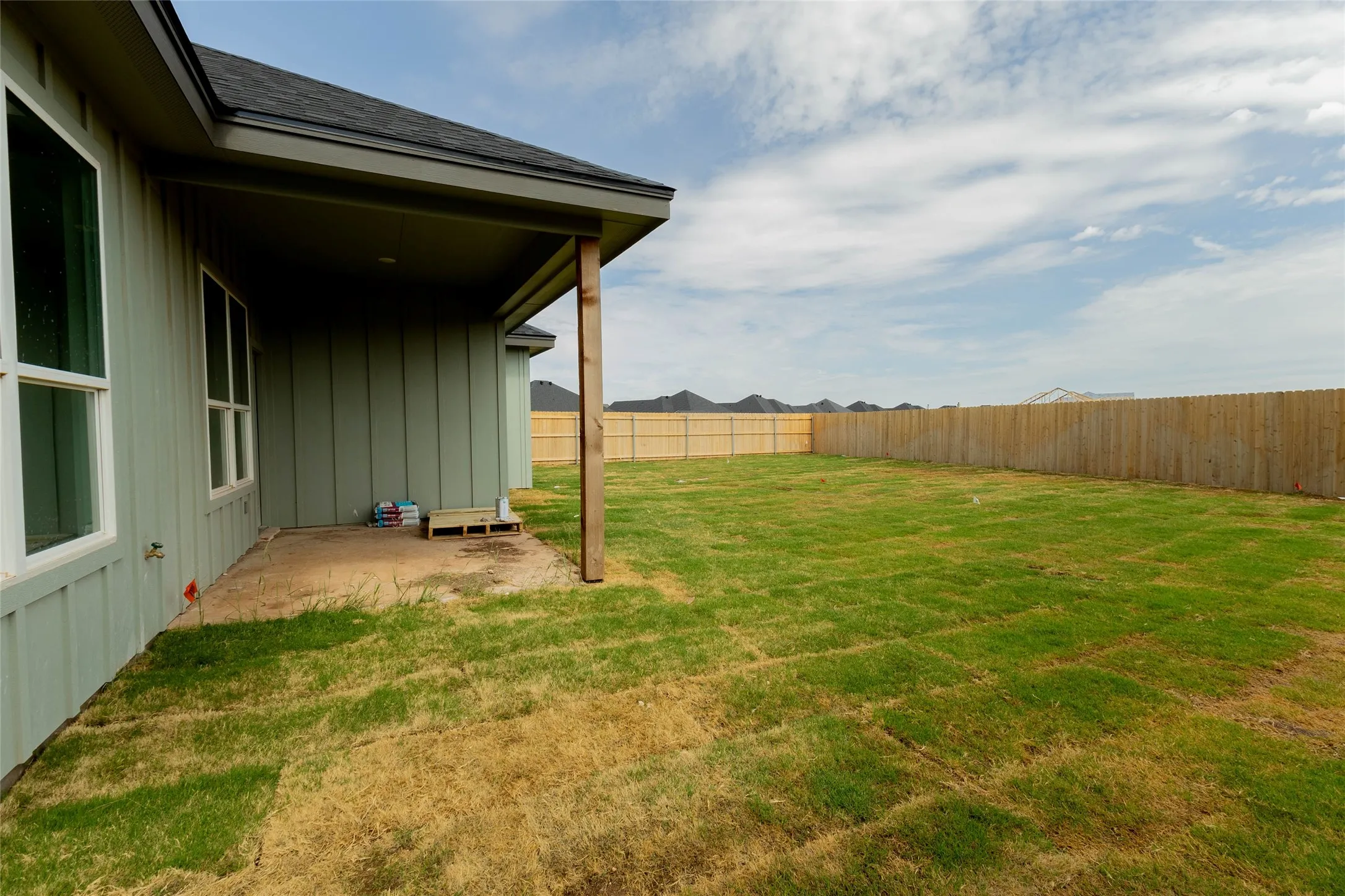 Expansive backyard featuring newly laid sod, privacy fencing, and a covered patio area with a wood support beam
