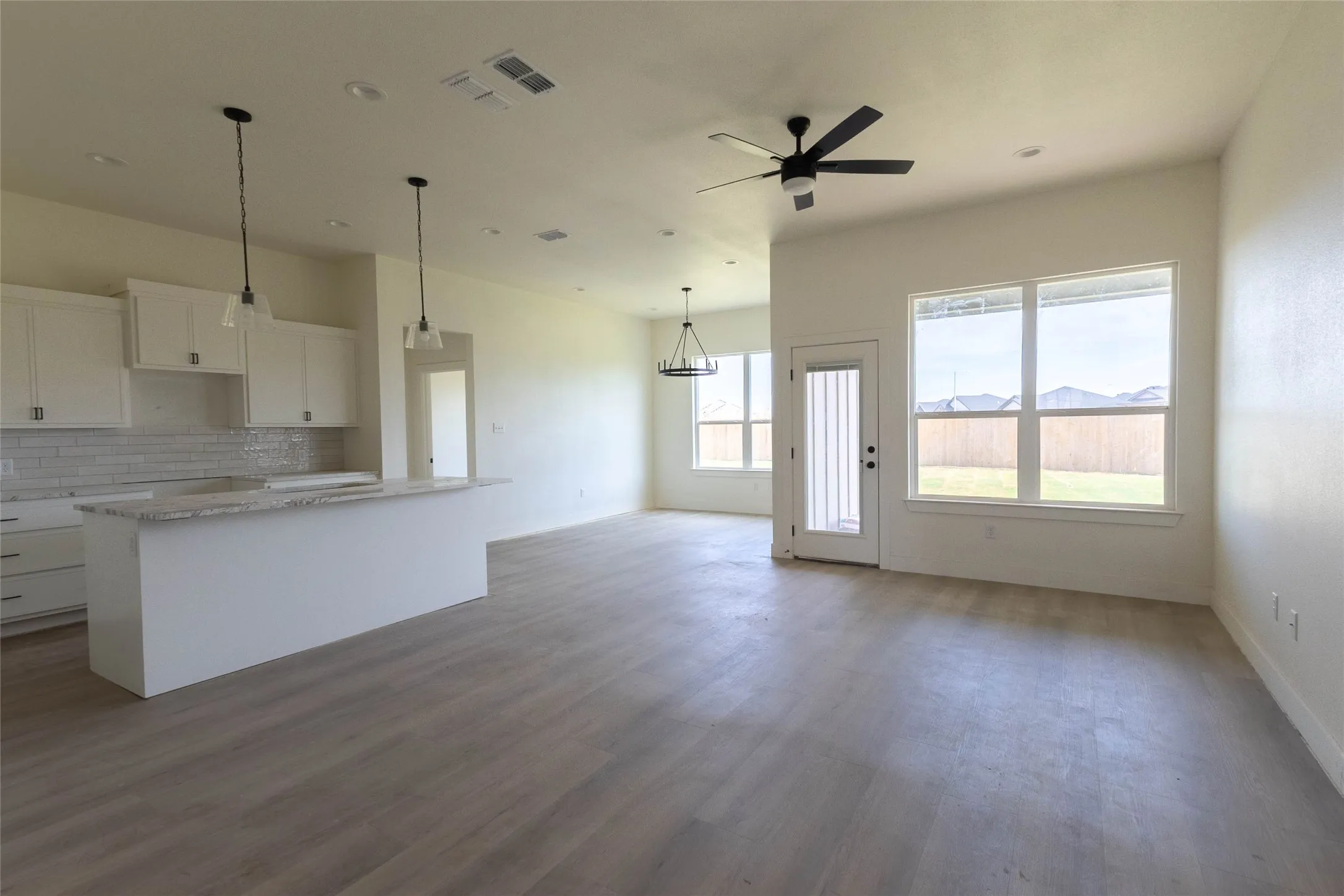 Open-concept living space featuring wood-finish flooring, white cabinetry, a kitchen island with a light-colored countertop, and a ceiling fan
