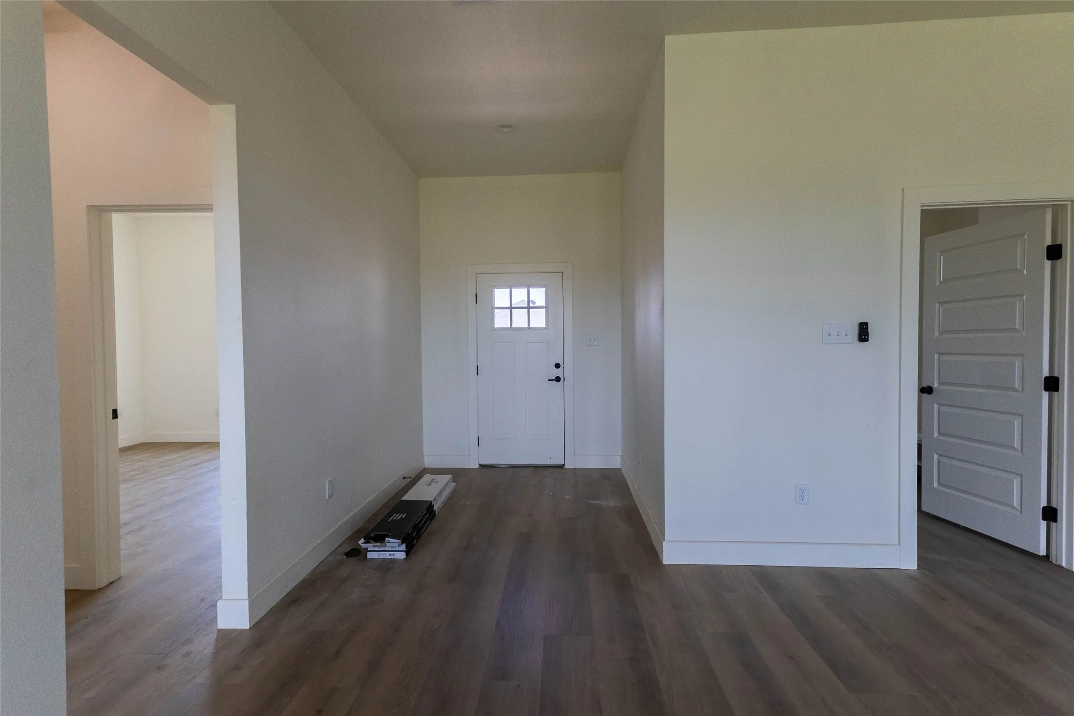 Entryway featuring wood-finish flooring, a white paneled door with window panes, and interior doors with black hardware