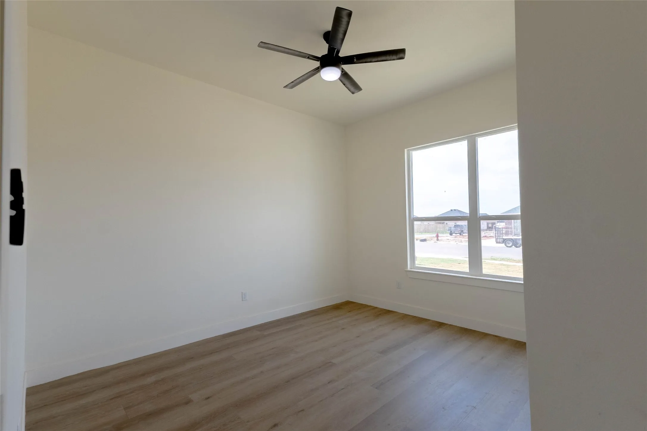 Wood-finish flooring with crisp white walls, a large window, and a ceiling fan with integrated lighting