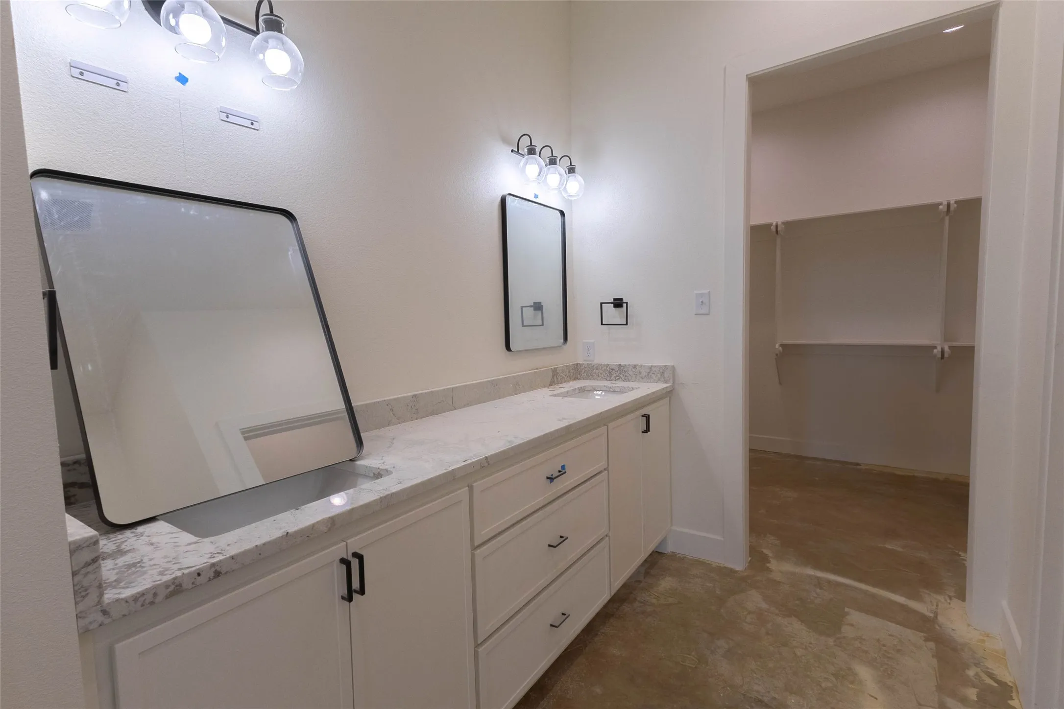 Dual vanity with integrated sinks, light-toned stone countertop, white shaker-style cabinetry with matte black hardware, and wall-mounted light fixtures
